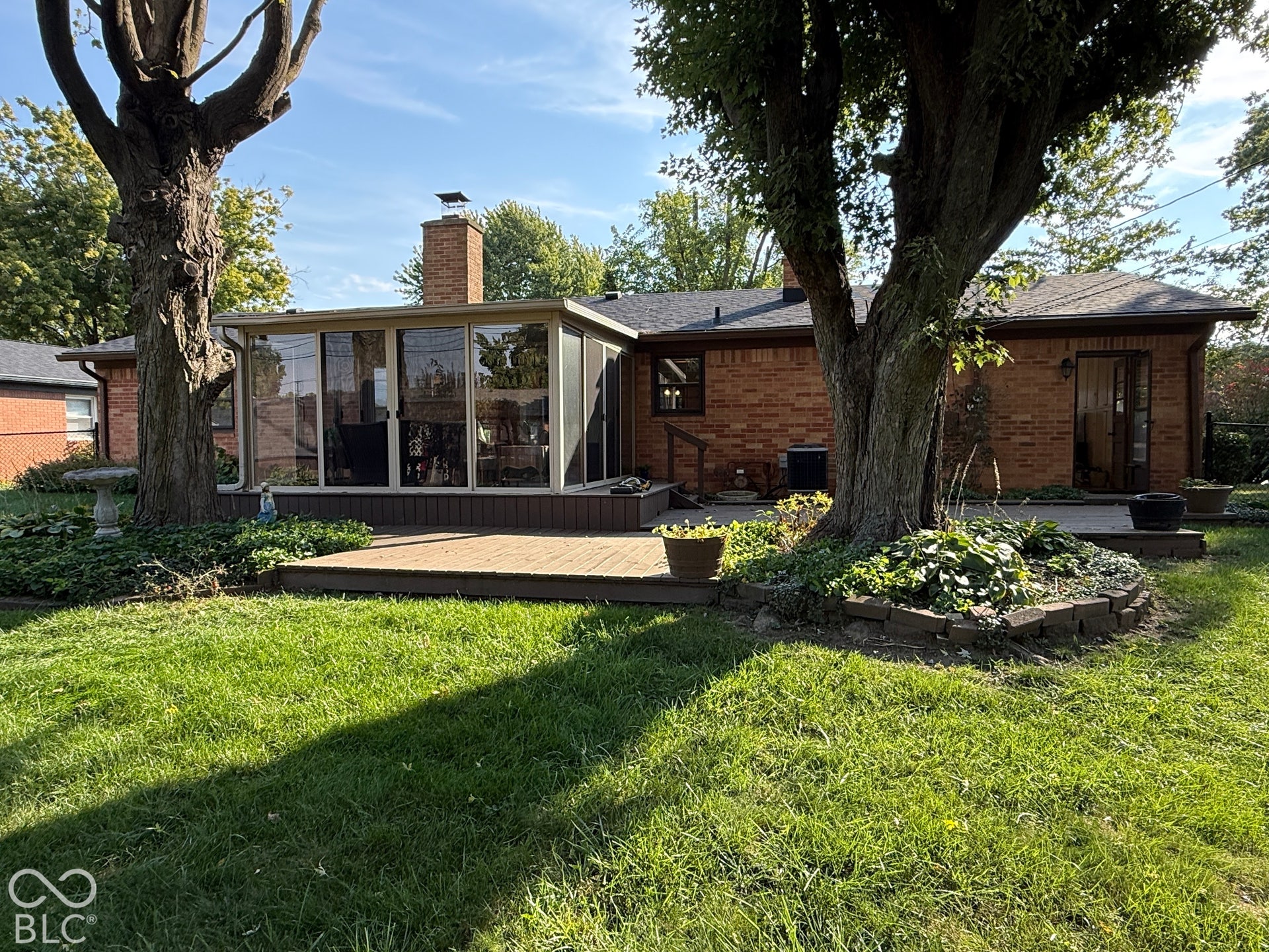 Brick exterior featuring a sunroom addition, wood deck, and mature trees