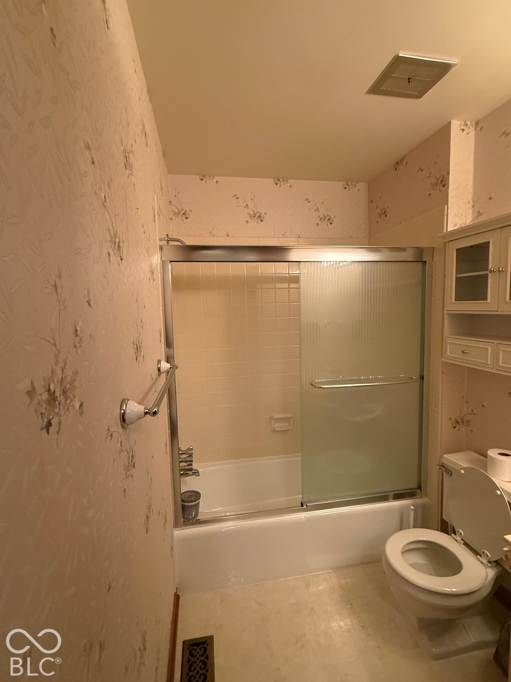 Bathroom featuring a white bathtub with a sliding glass enclosure, white toilet, and built-in cabinetry with glass-front uppers