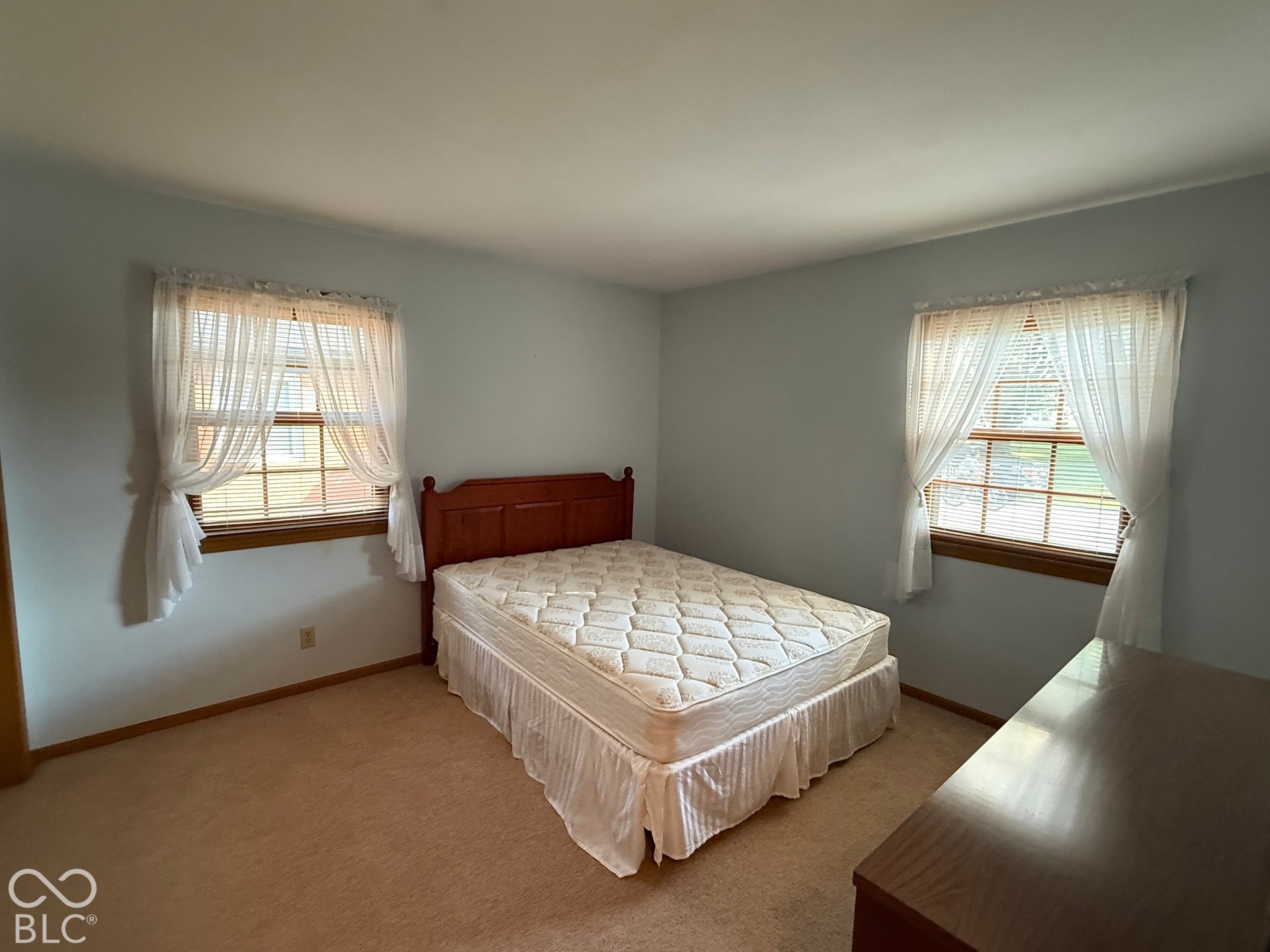 Wall-to-wall carpeting, two windows with wood trim, and light blue walls