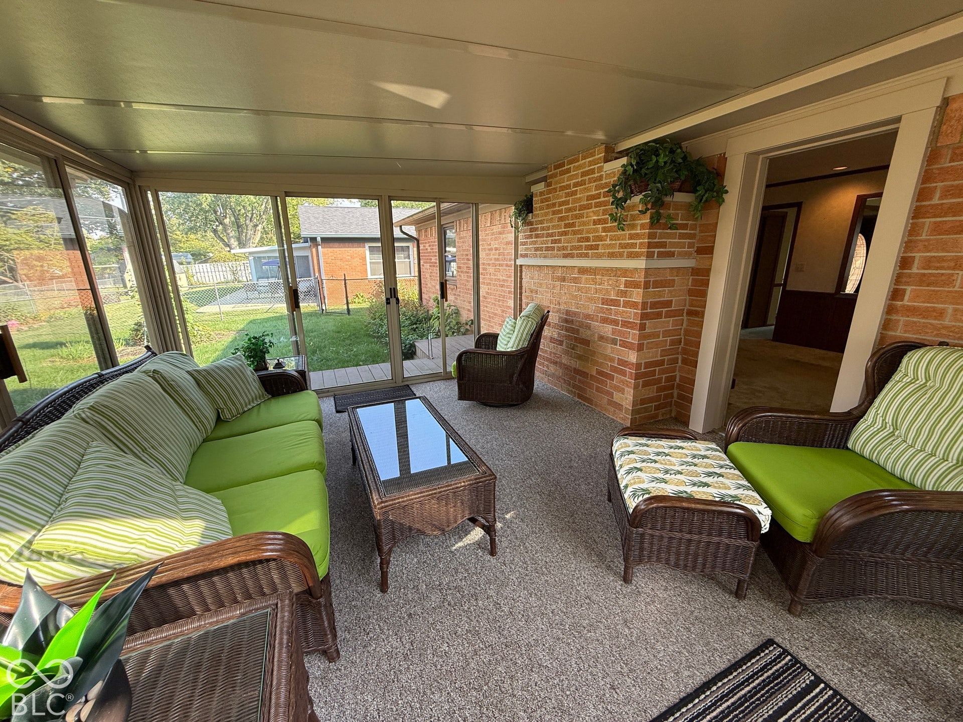 Enclosed porch with multiple sliding glass panels, light-colored ceiling, and carpeted flooring