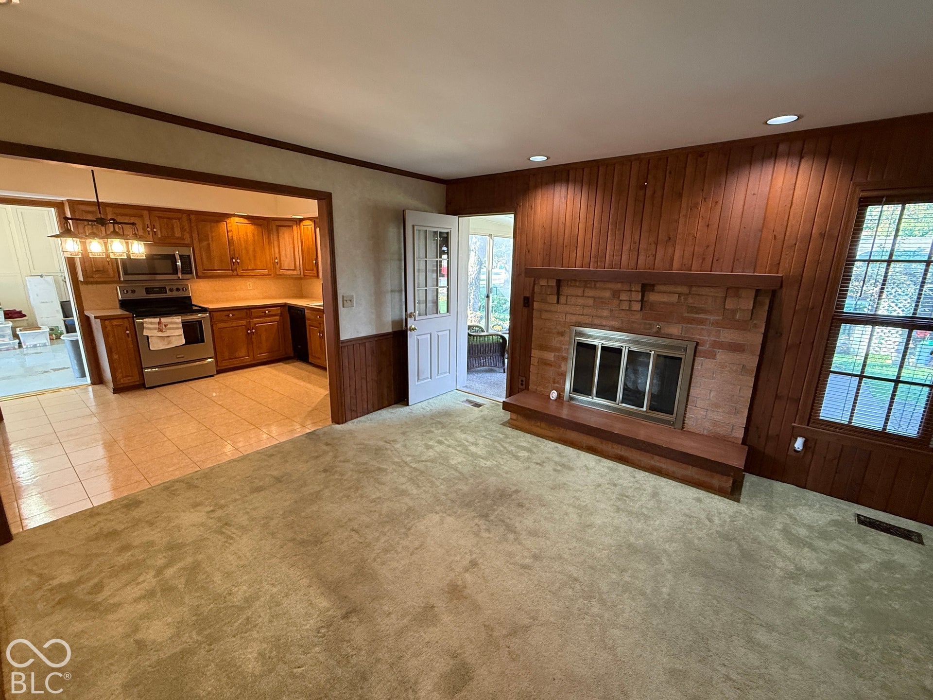 Brick fireplace with a wood mantle, wood-paneled walls, and recessed lighting