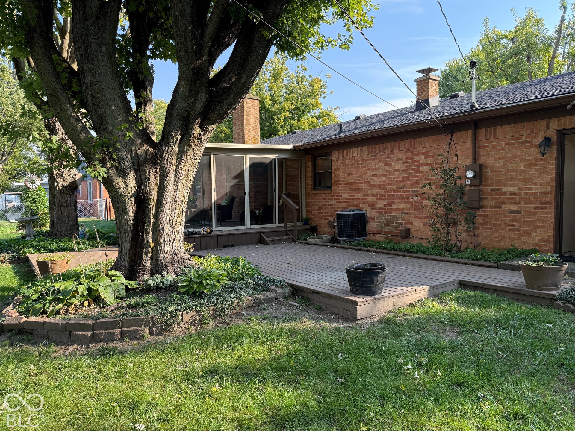 Brick exterior with a wood deck, enclosed patio, and mature trees