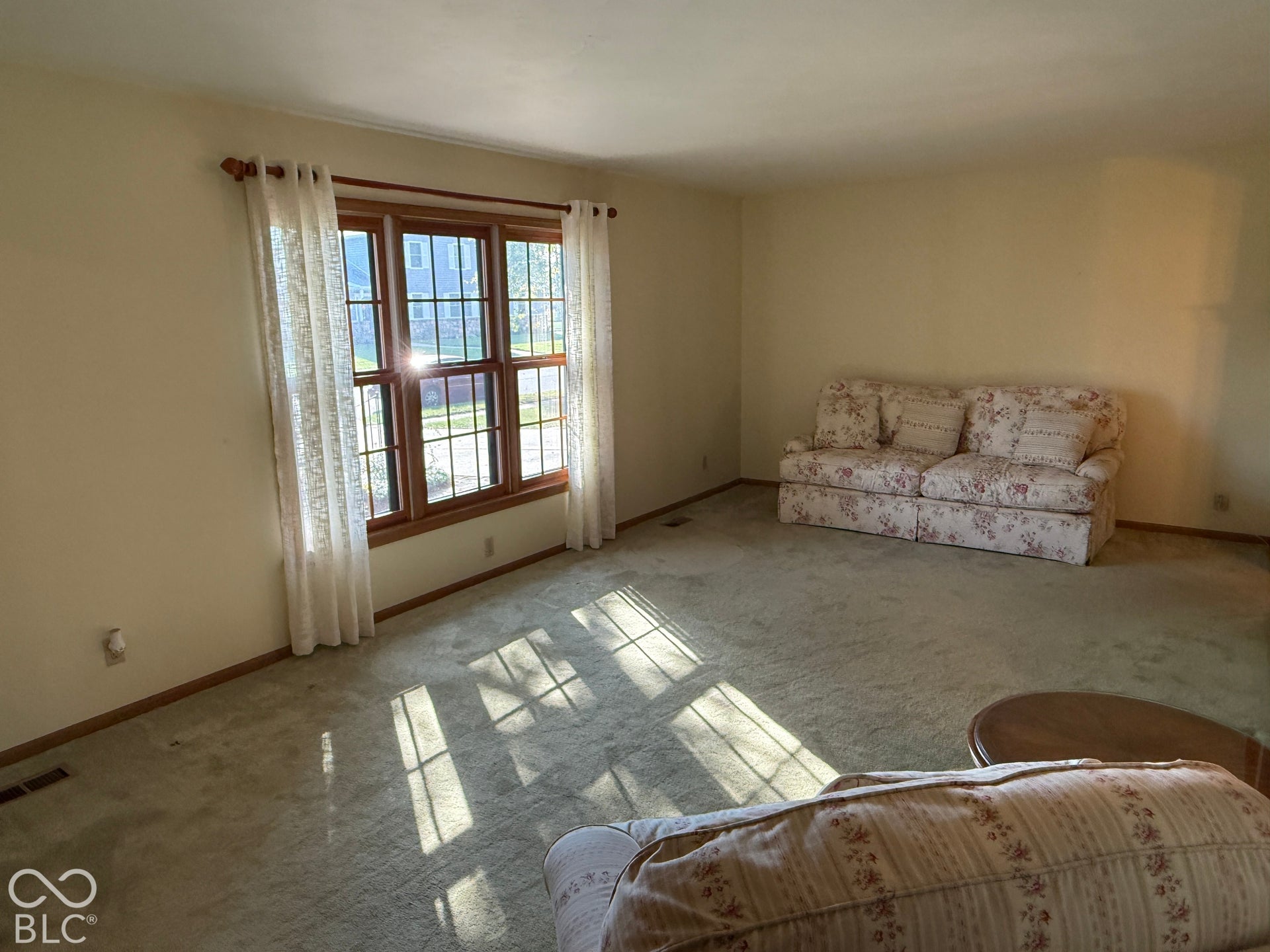 Expansive interior with light-colored carpeting, warm-toned wall paint, and a large multi-pane window featuring wood trim