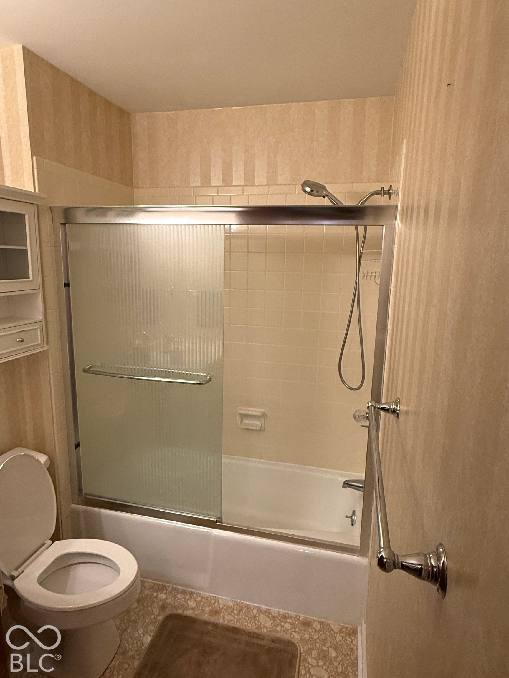Tub and shower combination with sliding frosted glass doors, tiled surround, and integrated showerhead