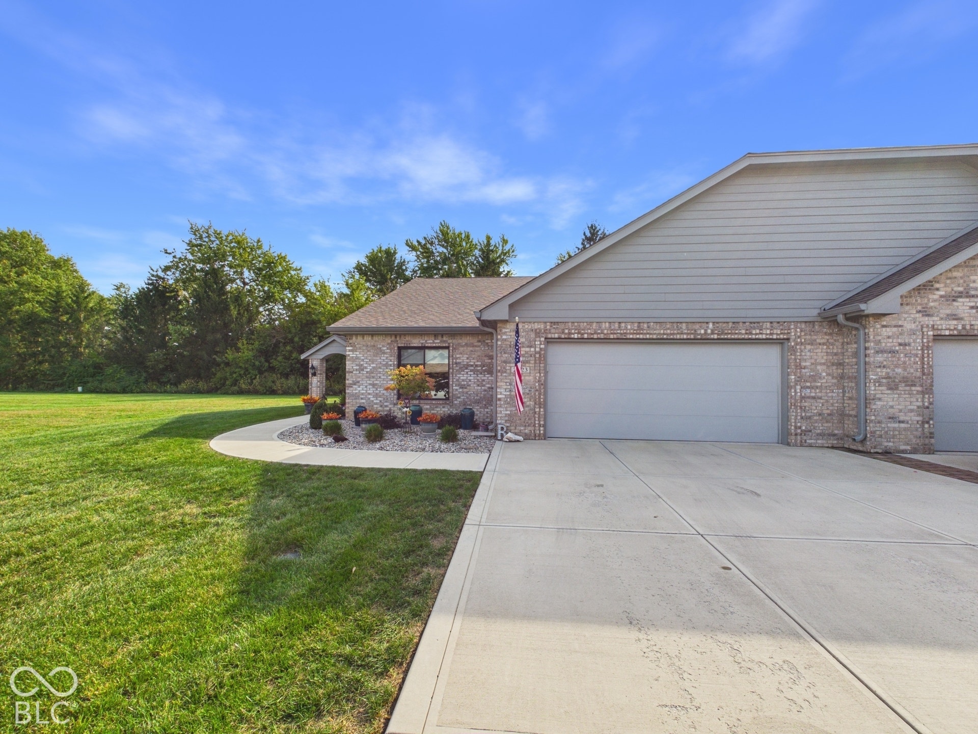 Brick exterior with gray siding accents, attached garage with light gray door, concrete driveway, concrete walkway, and a landscaped entry