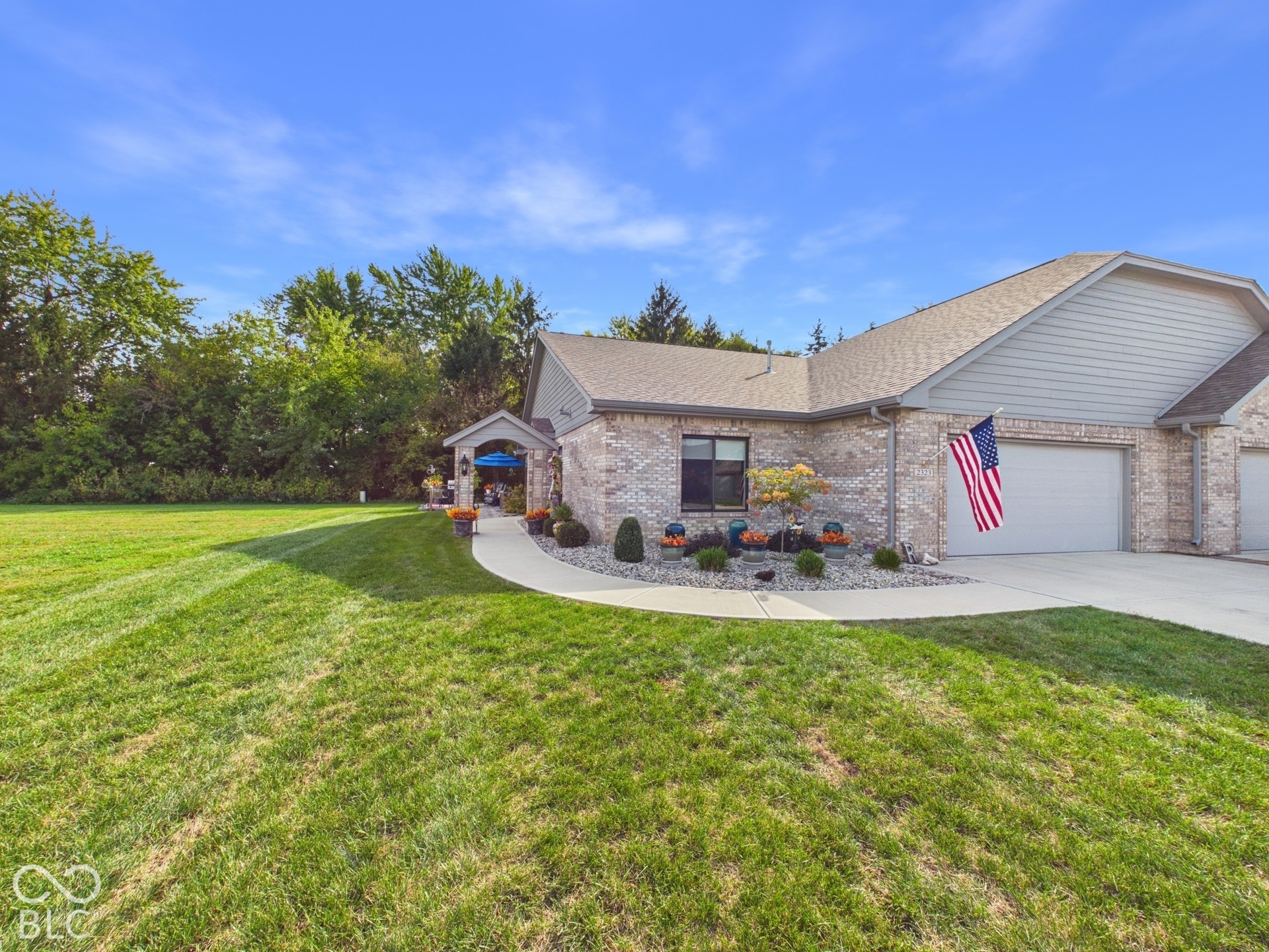 Brick exterior with light gray siding accents, mature landscaping, paved driveway, and covered entry