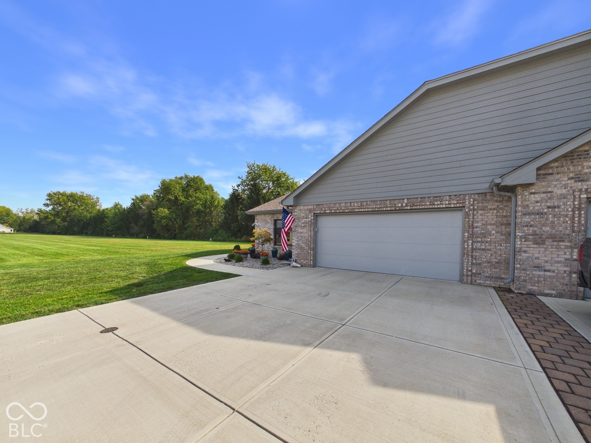 Brick exterior with a gray garage door, concrete driveway, and expansive manicured lawn