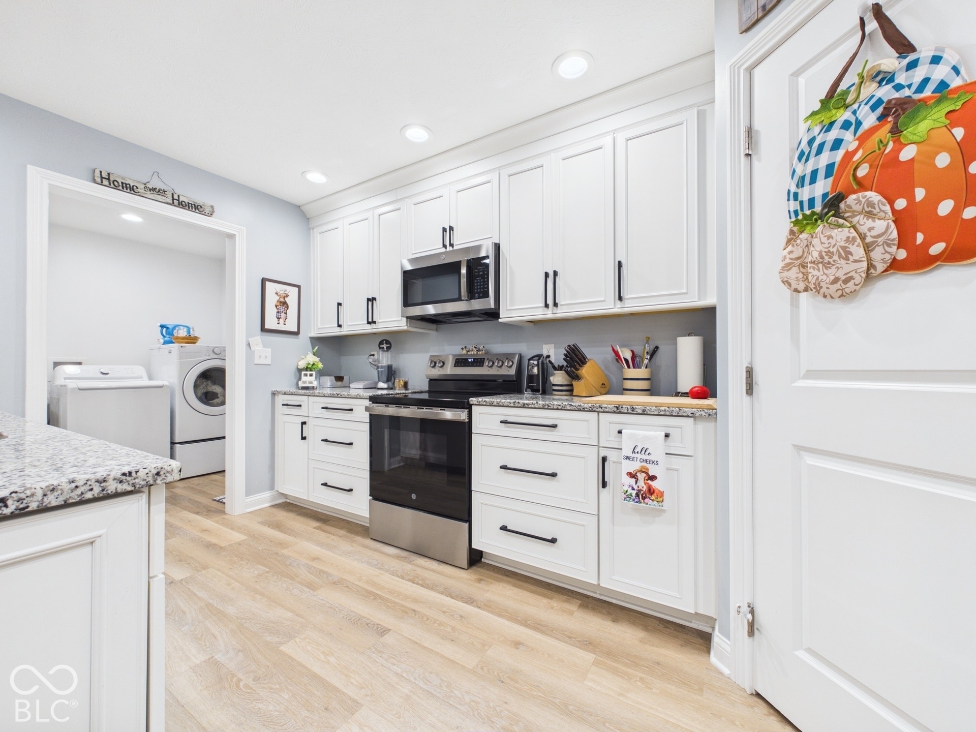 White shaker-style cabinetry with matte black hardware, stainless steel appliances including a range and microwave, light wood-finish flooring, and recessed ceiling lighting