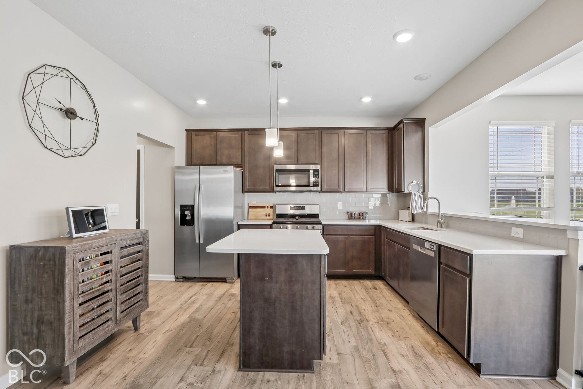 Kitchen featuring a central island, white quartz countertops, dark cabinetry, light gray subway tile backsplash, and stainless steel appliances