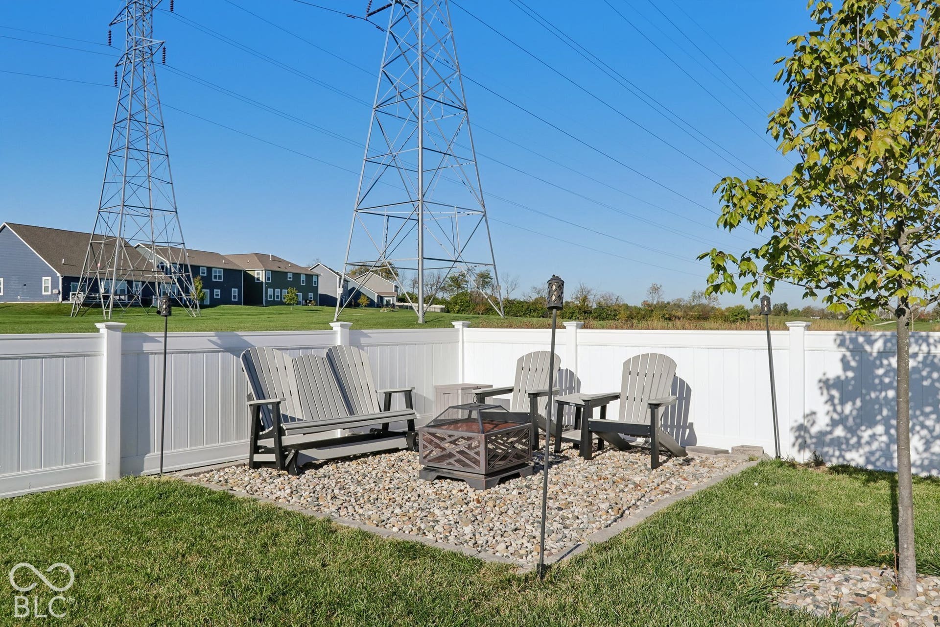 Enclosed backyard featuring a white privacy fence, a gravel patio area with a fire pit