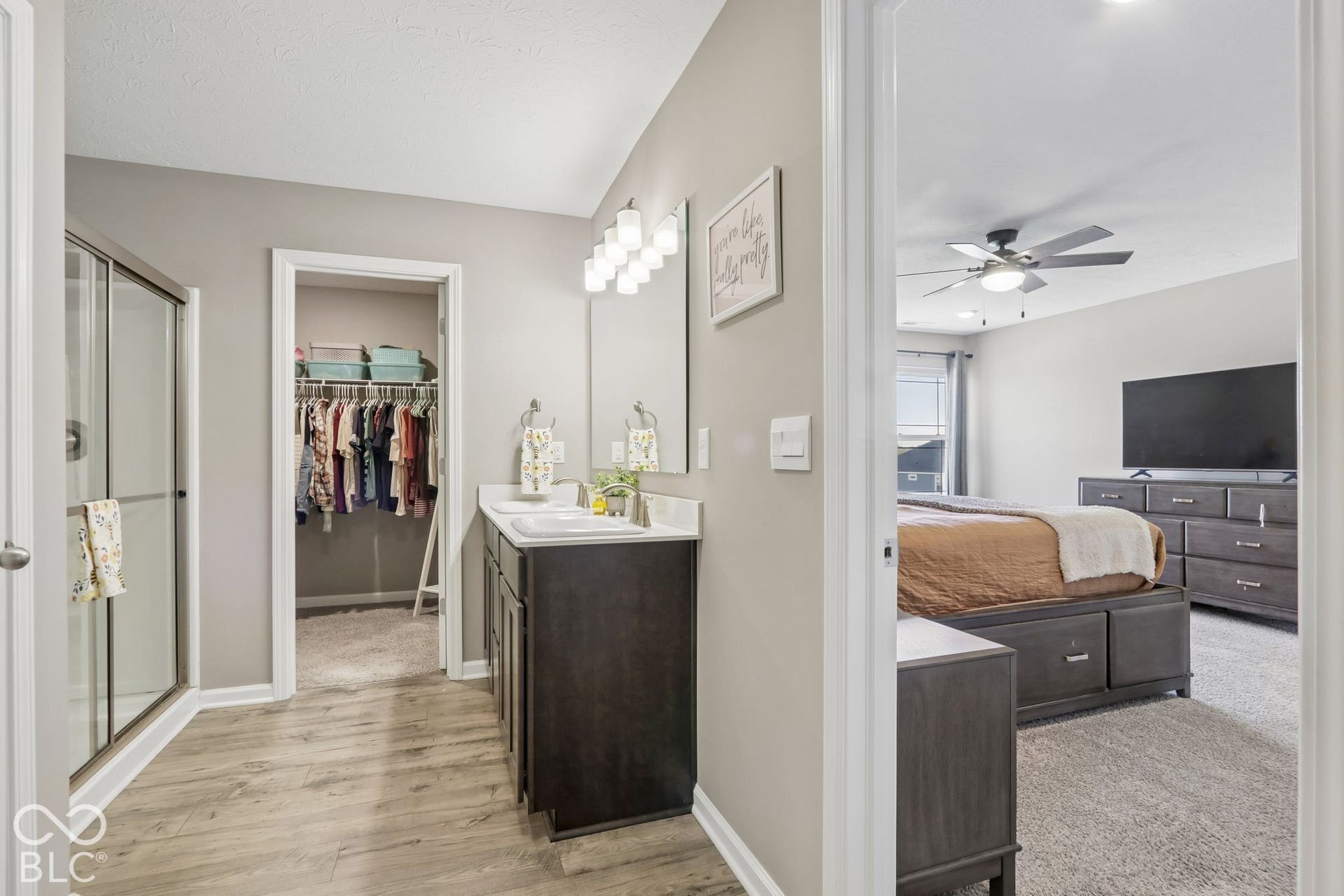 Dual vanity with dark cabinetry, glass-enclosed shower, and 2 walk-in closets