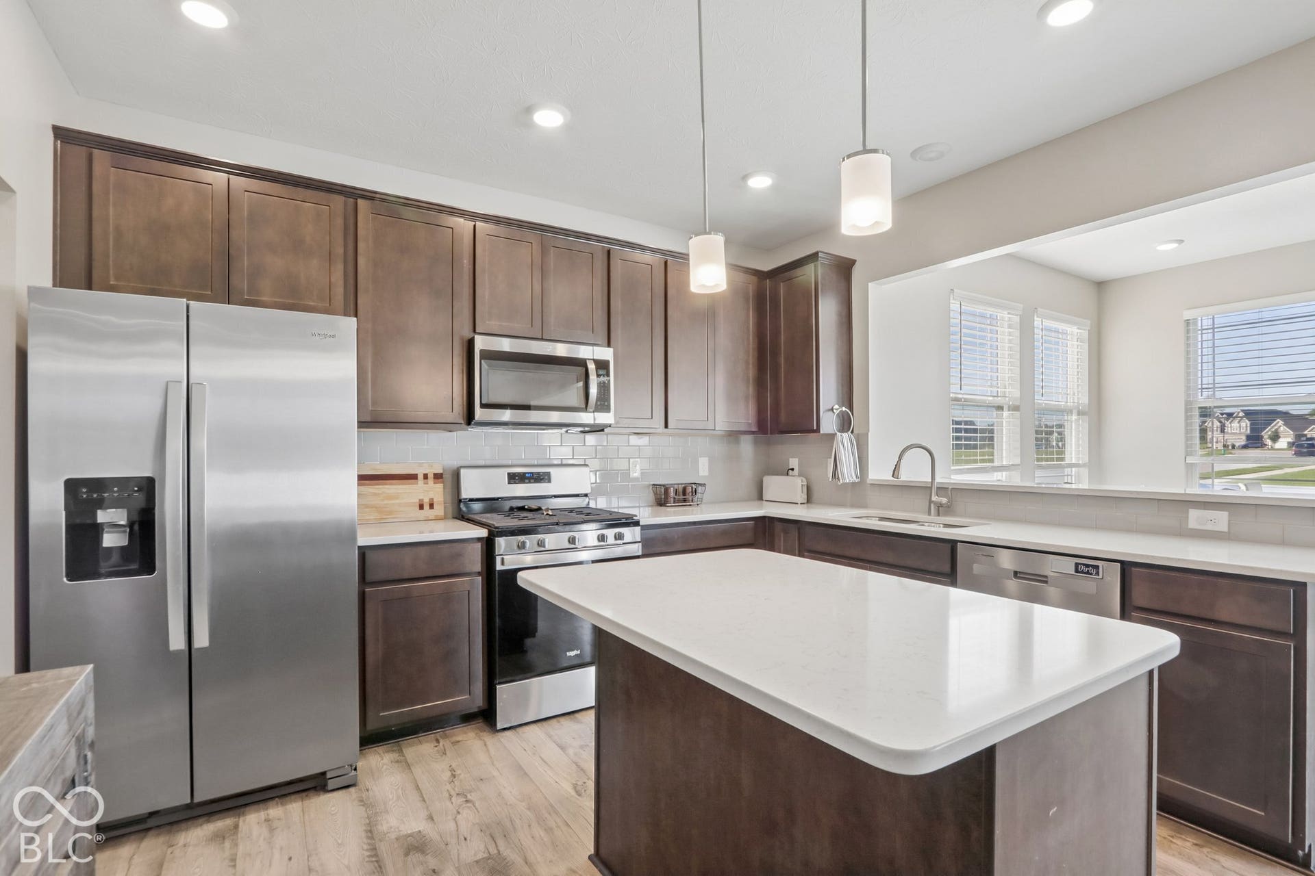 Kitchen featuring a central island, white quartz countertops, dark cabinetry, light gray subway tile backsplash, and stainless steel appliances
