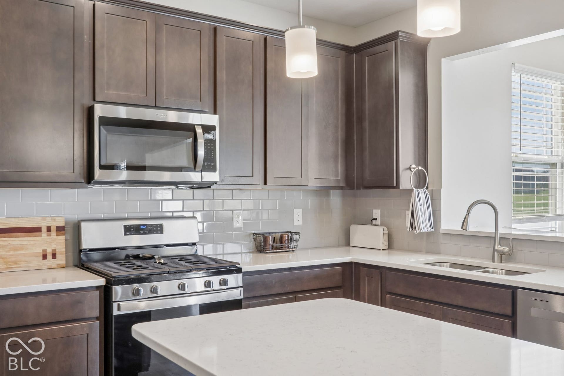 Kitchen featuring a central island, white quartz countertops, dark cabinetry, light gray subway tile backsplash, and stainless steel appliances