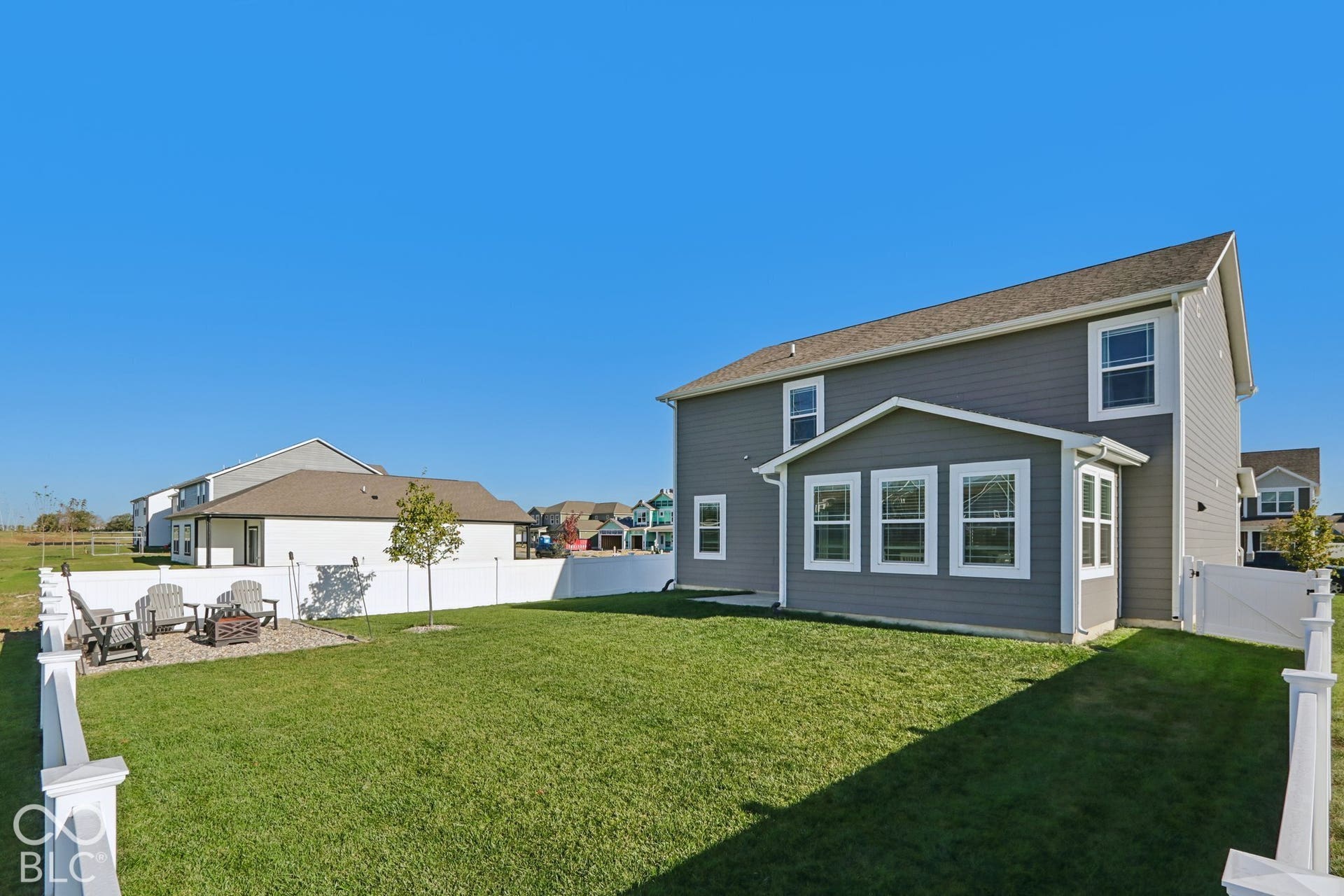 Expansive backyard featuring a manicured lawn, white privacy fence, and a stone-paved patio with a built-in fire pit