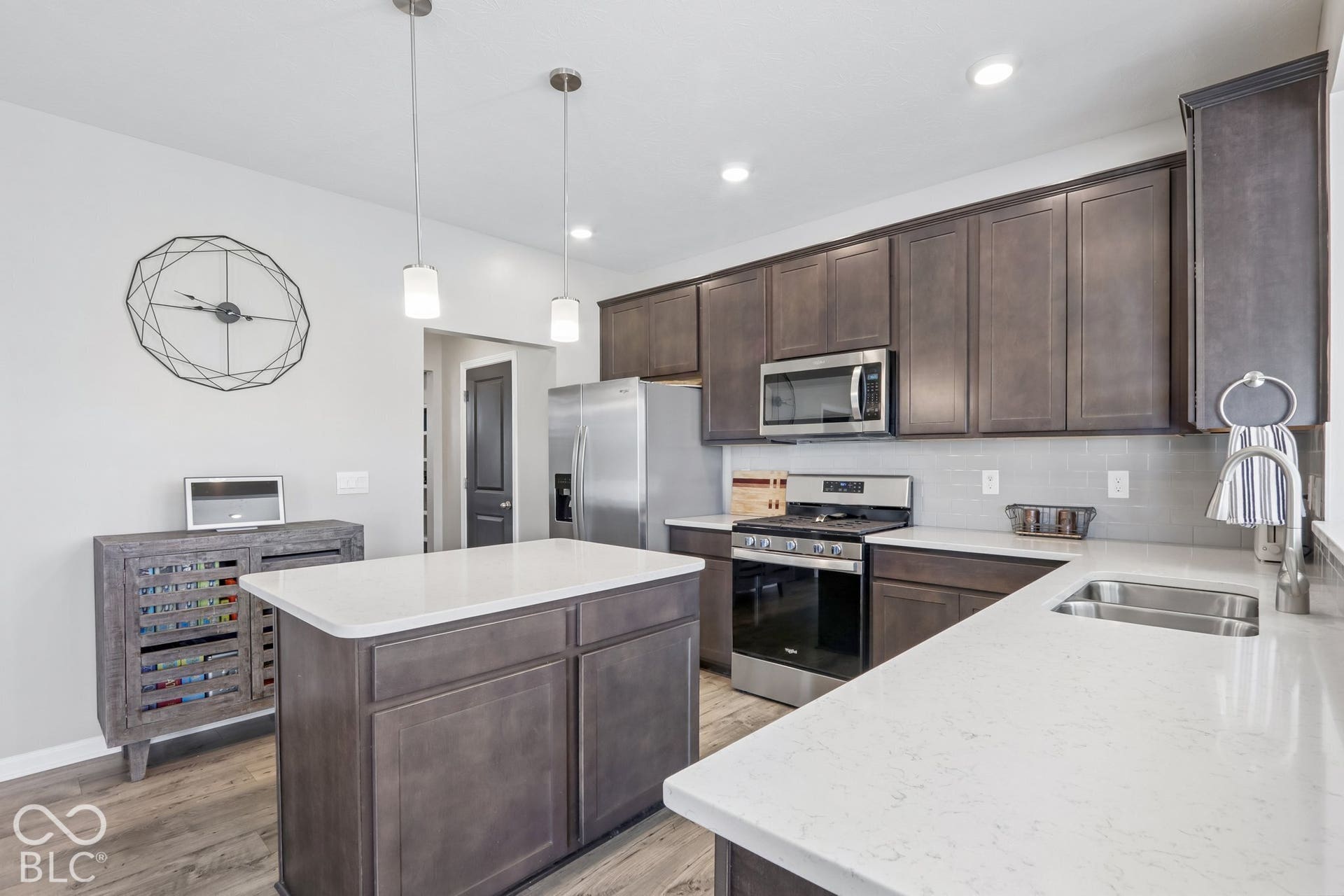 Kitchen featuring a central island, white quartz countertops, dark cabinetry, light gray subway tile backsplash, and stainless steel appliances