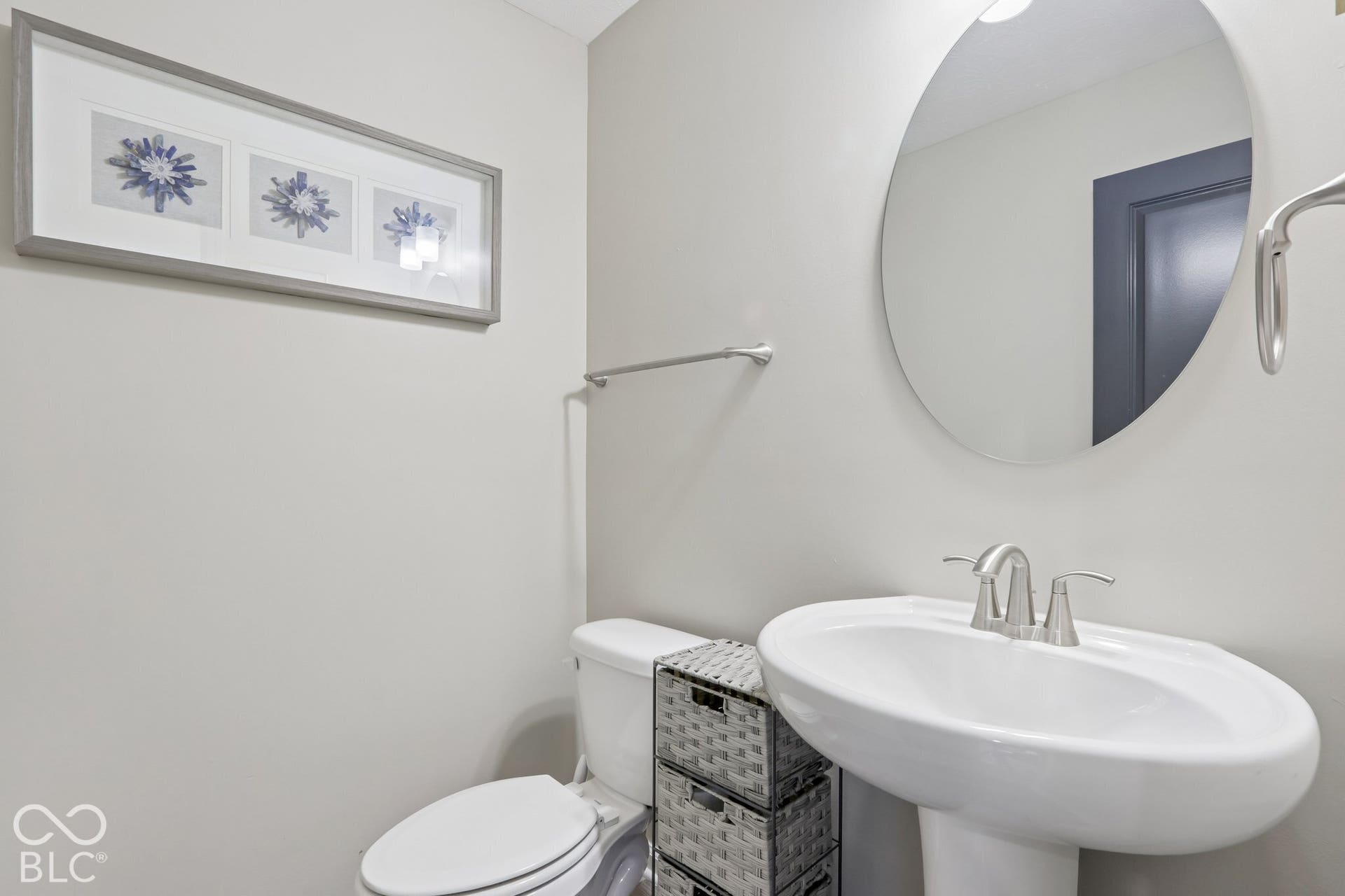 Half bathroom on main floor, with pedestal sink with a polished chrome faucet, round wall-mounted mirror