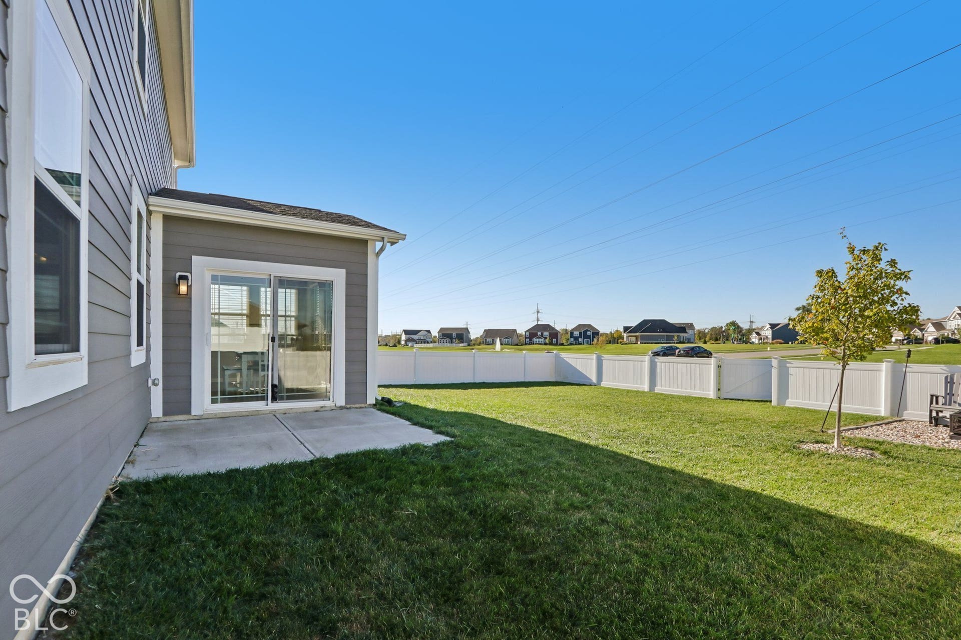 Expansive green lawn with a white privacy fence, concrete patio, and sliding glass doors