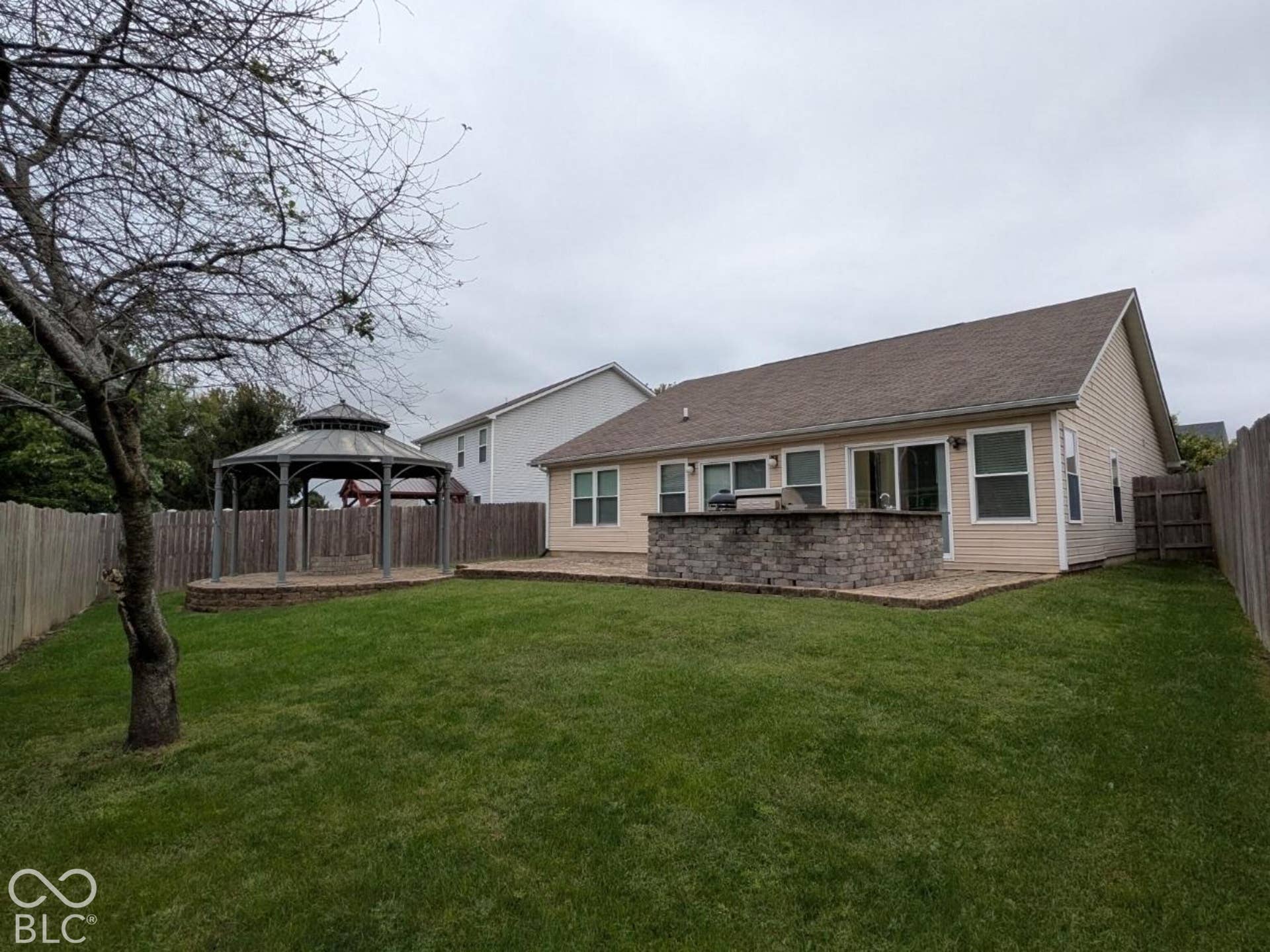Expansive backyard featuring a lush lawn, privacy fence, and a patio with a built-in stone-finish bar