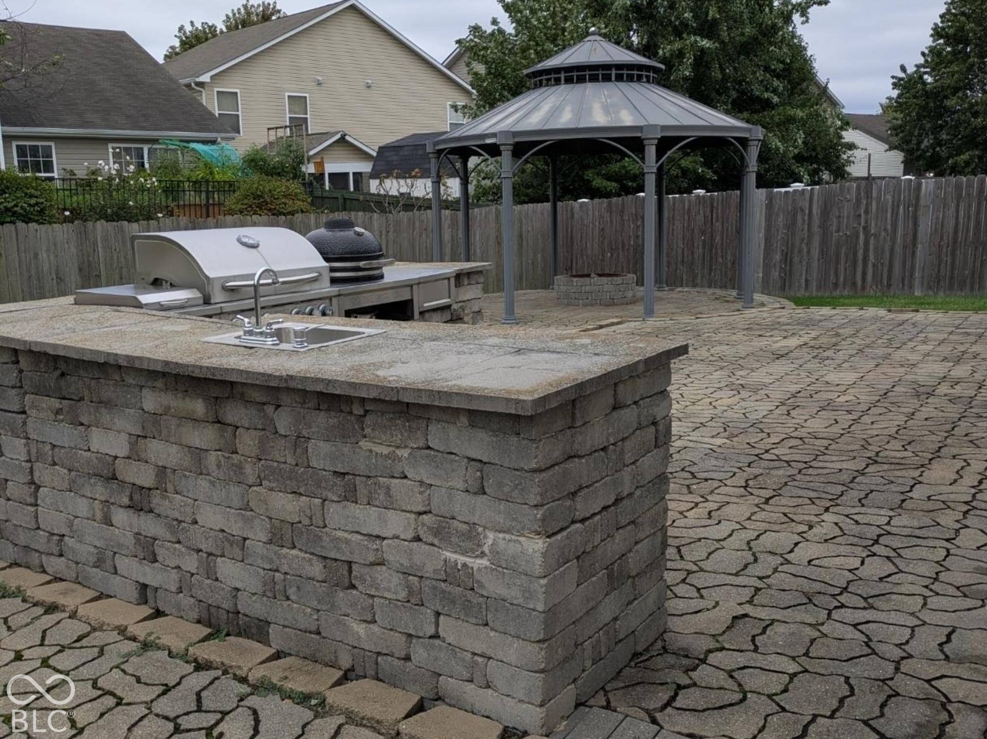 Outdoor kitchen featuring a built-in grill, sink, and stone-finish base