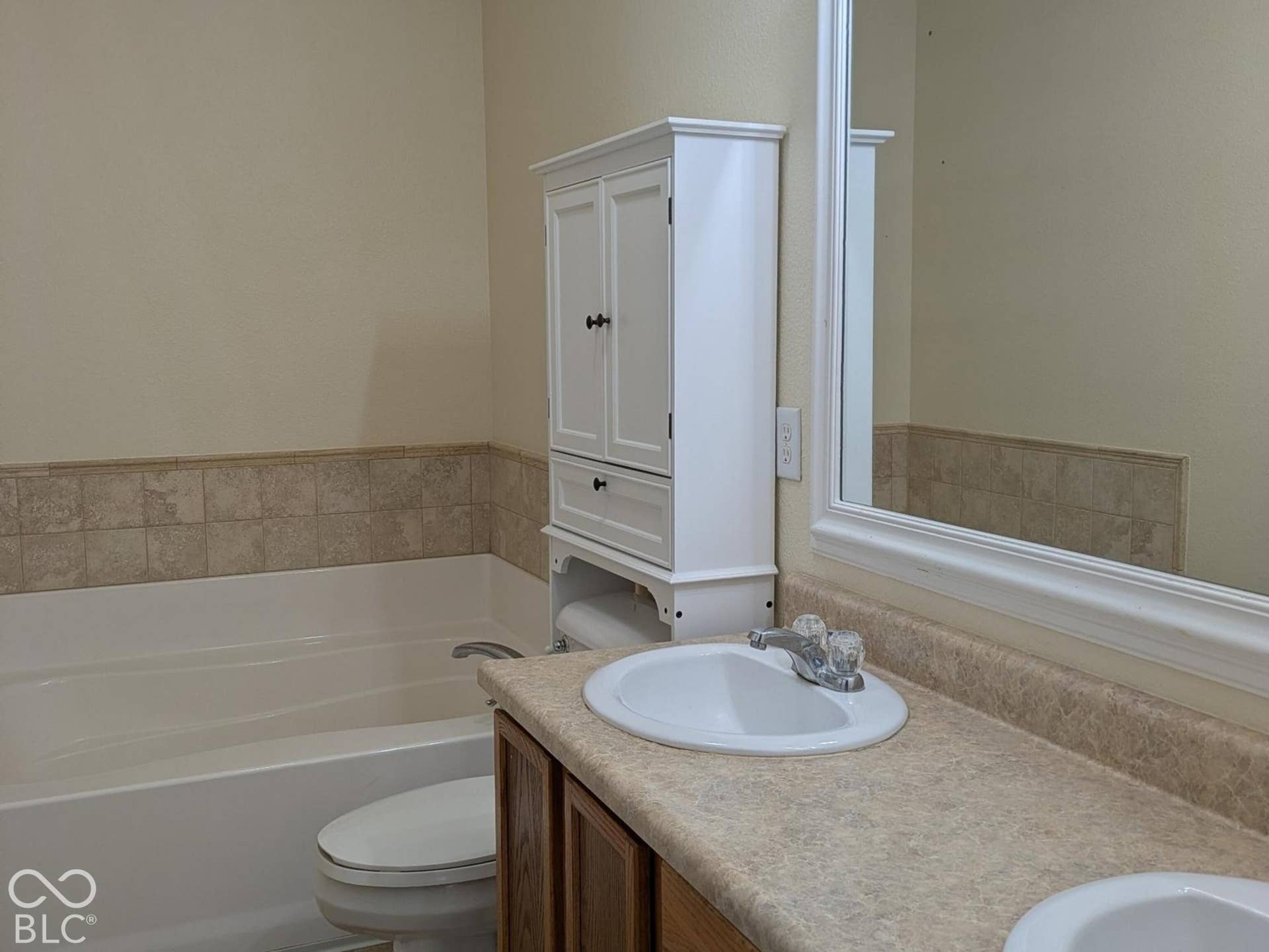 Double vanity with integrated sinks, wood-finish cabinetry, built-in bathtub, tile wainscoting, and tile flooring