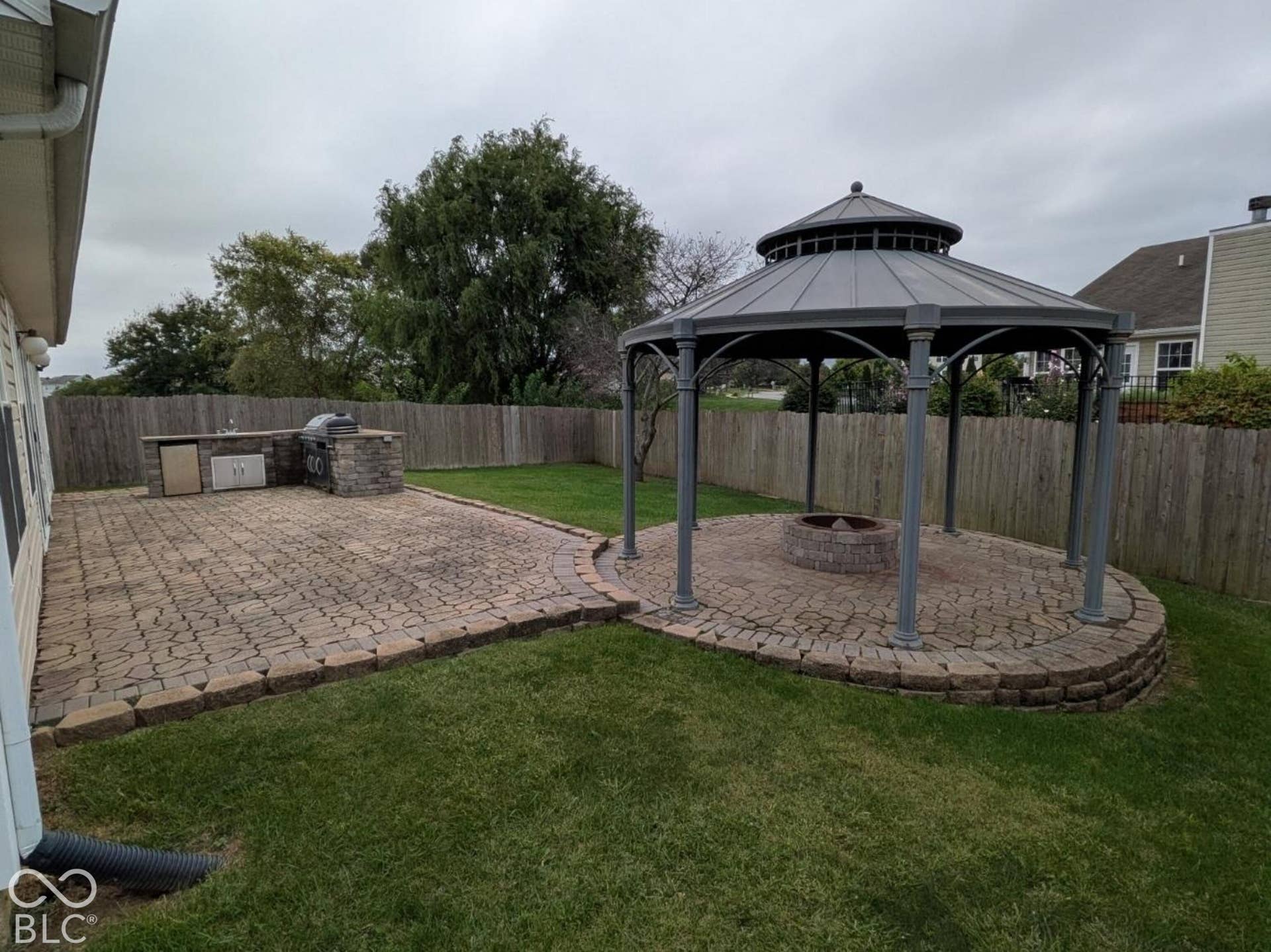 Expansive backyard featuring a stone paver patio, built-in outdoor kitchen, and a gazebo with a fire pit