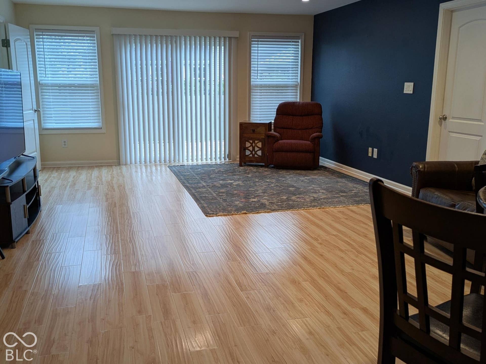 Recessed lighting, wood-finish flooring, sliding glass door with vertical blinds, multiple windows with horizontal blinds, and a bold accent wall