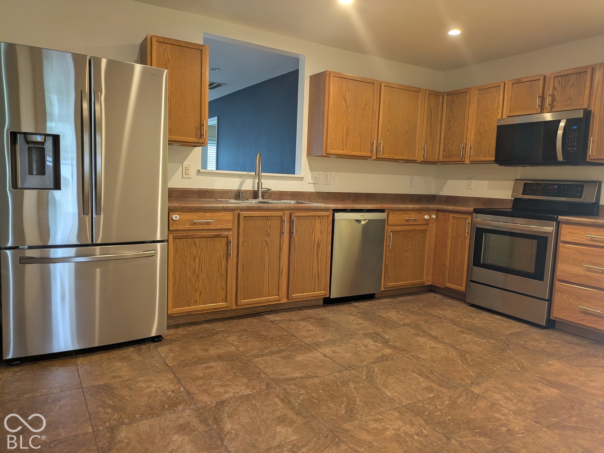 Kitchen featuring stainless steel appliances, wood cabinetry, tile flooring, and a double-basin sink