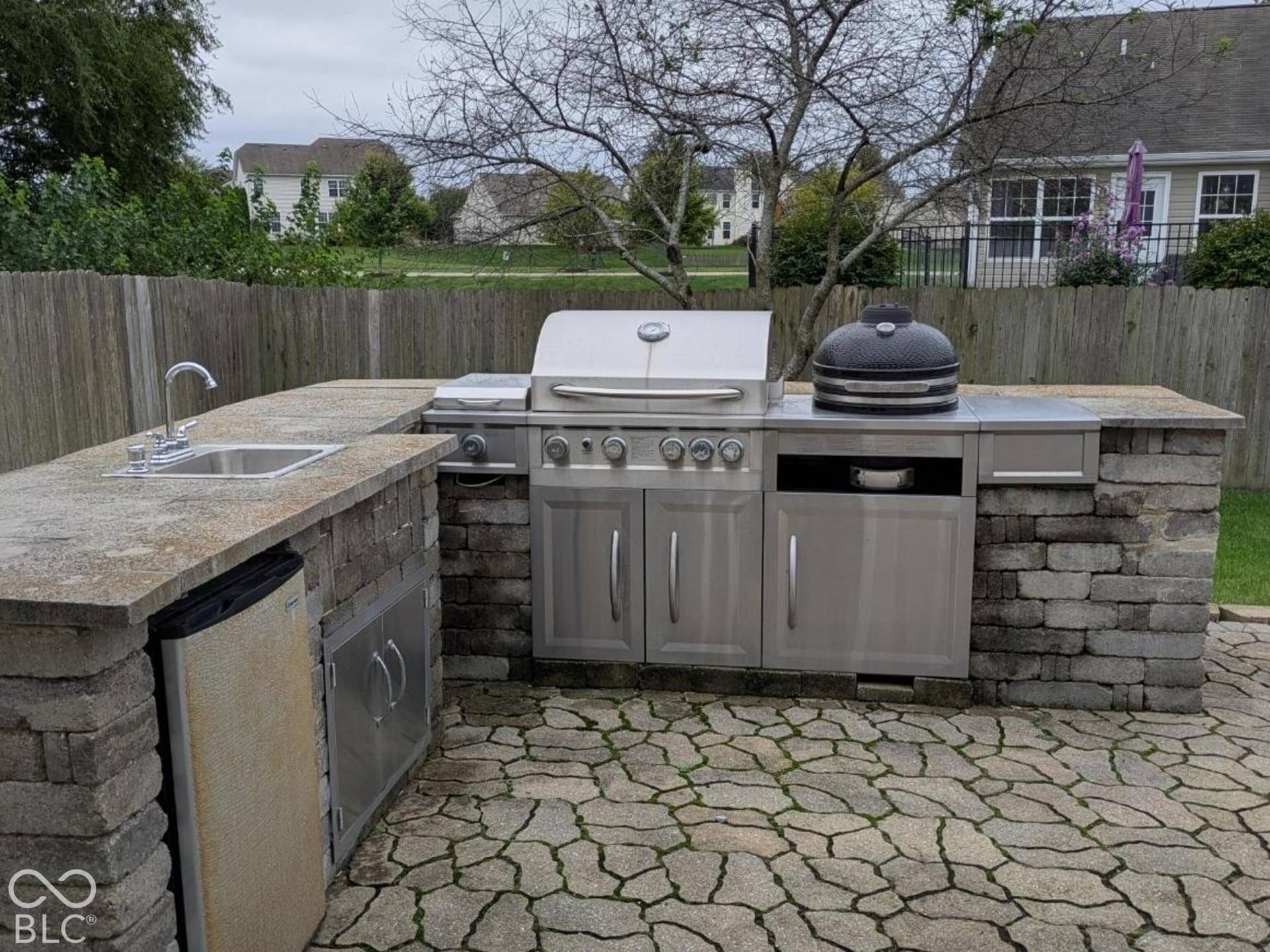 Outdoor kitchen featuring a built-in grill, integrated sink, stainless steel cabinetry, and stone block construction
