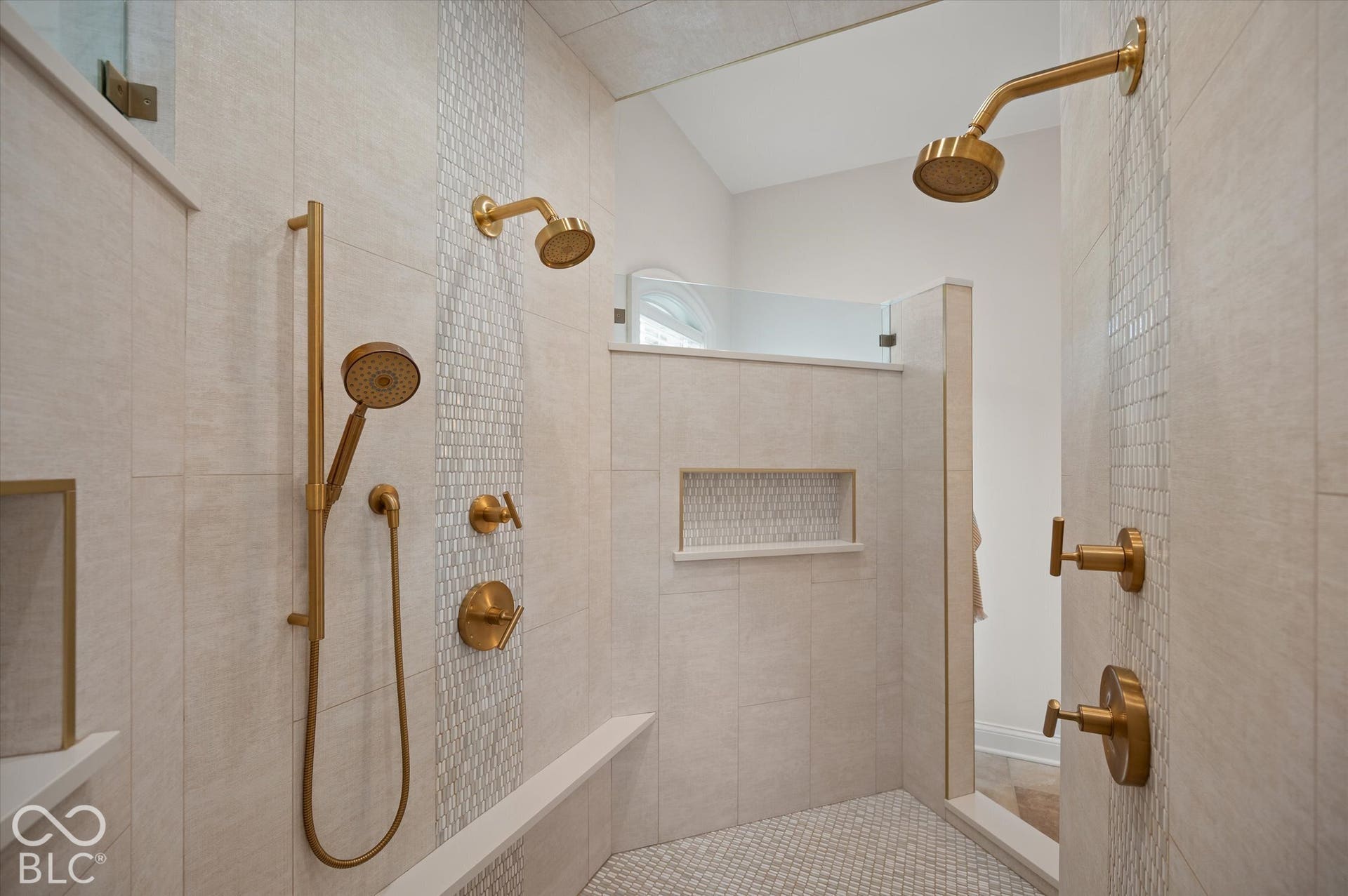 Tiled shower with multiple gold-finish shower heads, integrated bench, and mosaic tile accents