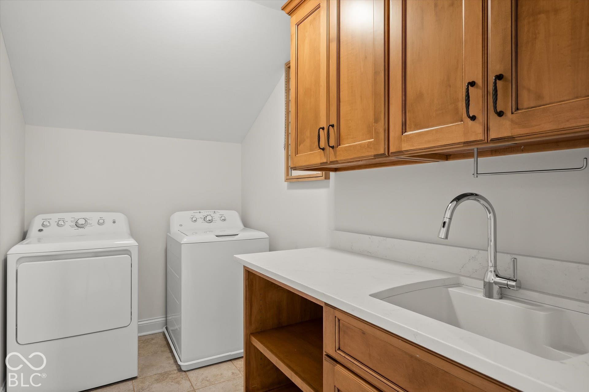 Laundry room with wood-finish cabinetry, white countertop, and a built-in sink with a gooseneck faucet
