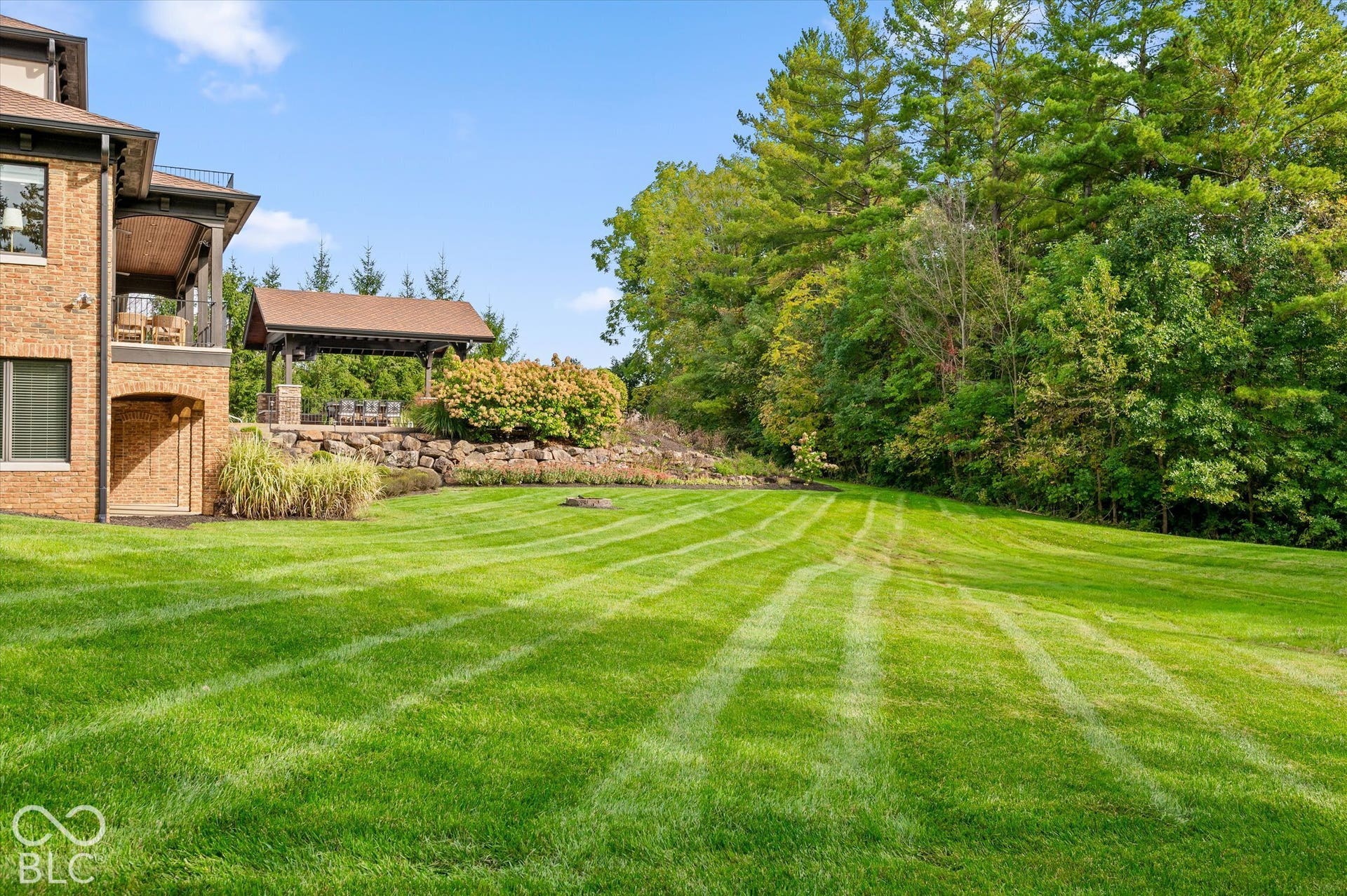 Expansive lawn with a covered outdoor entertaining area, extensive landscaping, and a brick exterior