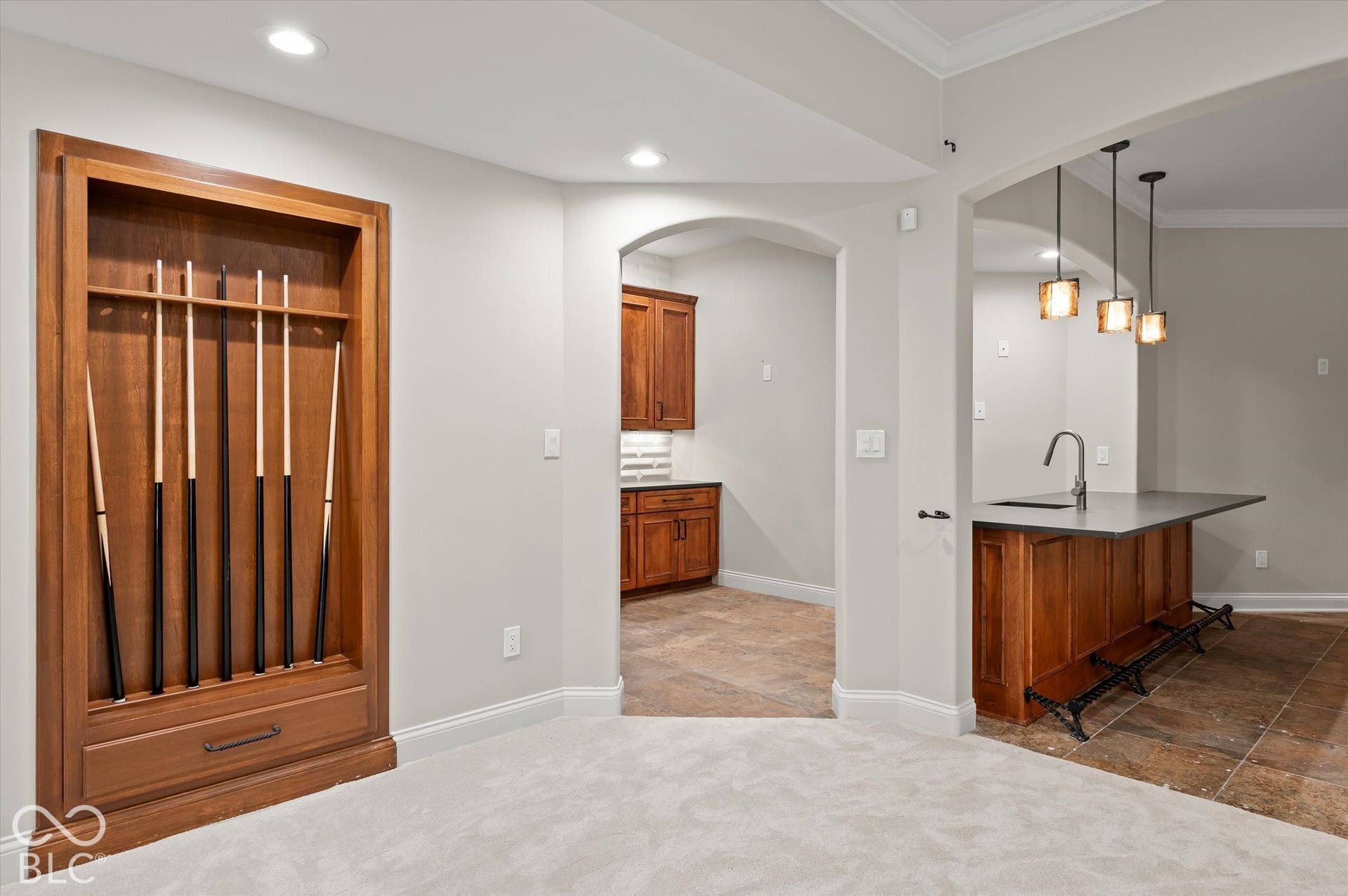 Built-in wooden cue rack, wet bar with a sink, pendant lighting, wood-finish cabinetry, and tiled flooring