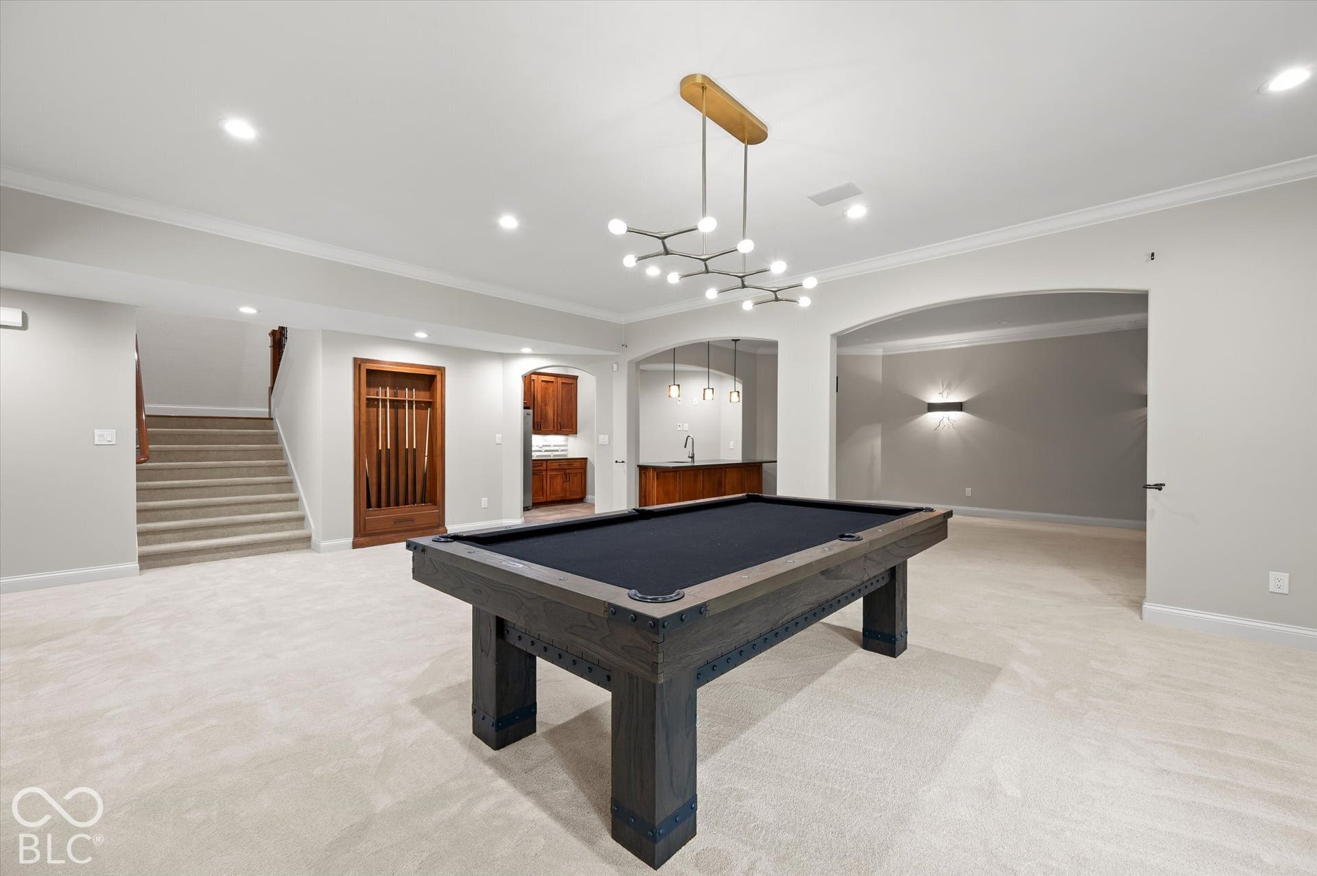 Spacious recreation area featuring a built-in wet bar, arched doorways, an accent wall with sconces, and recessed lighting