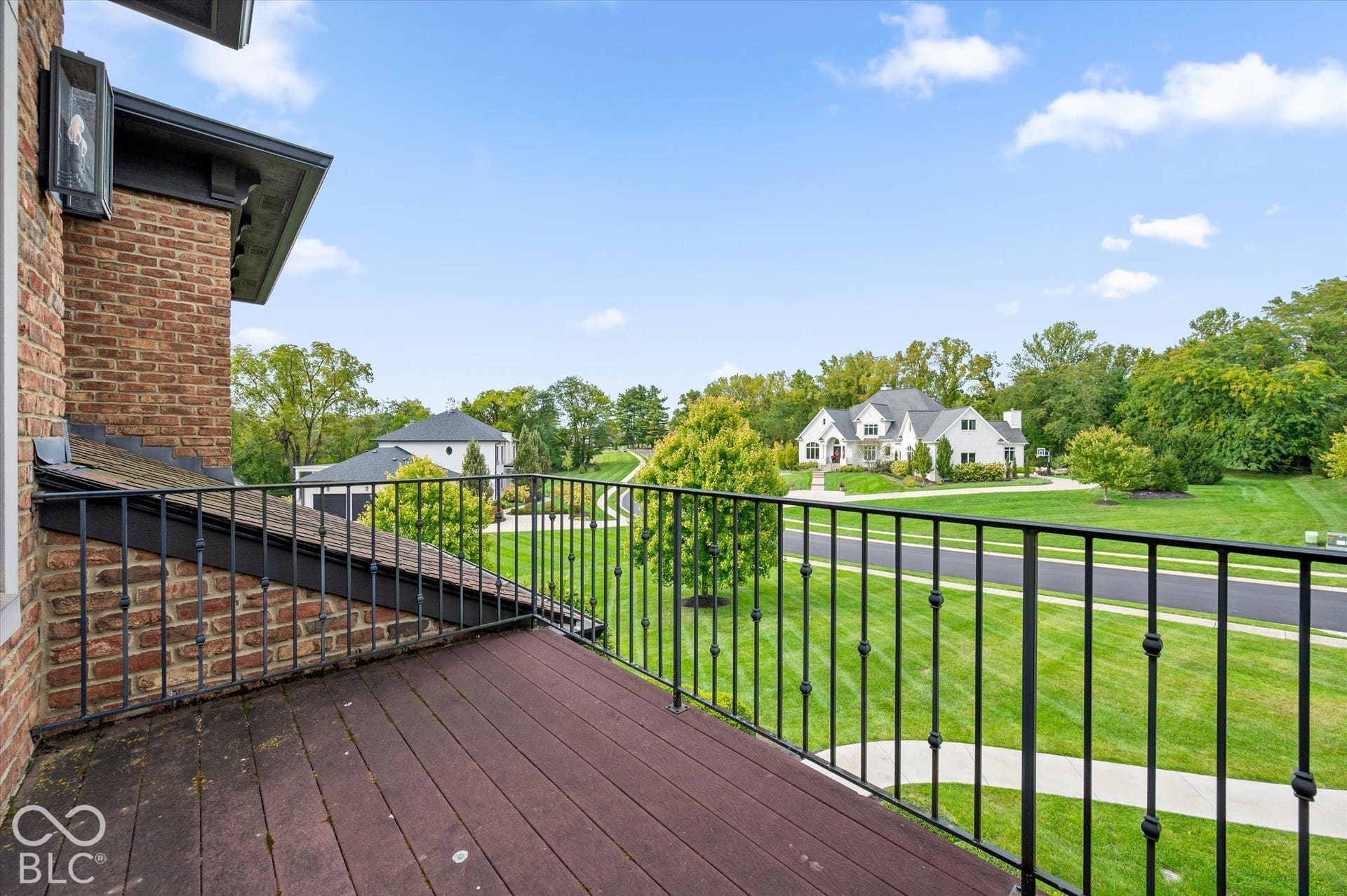 Brick exterior wall with an attached balcony featuring dark wood-finish decking and wrought iron railing