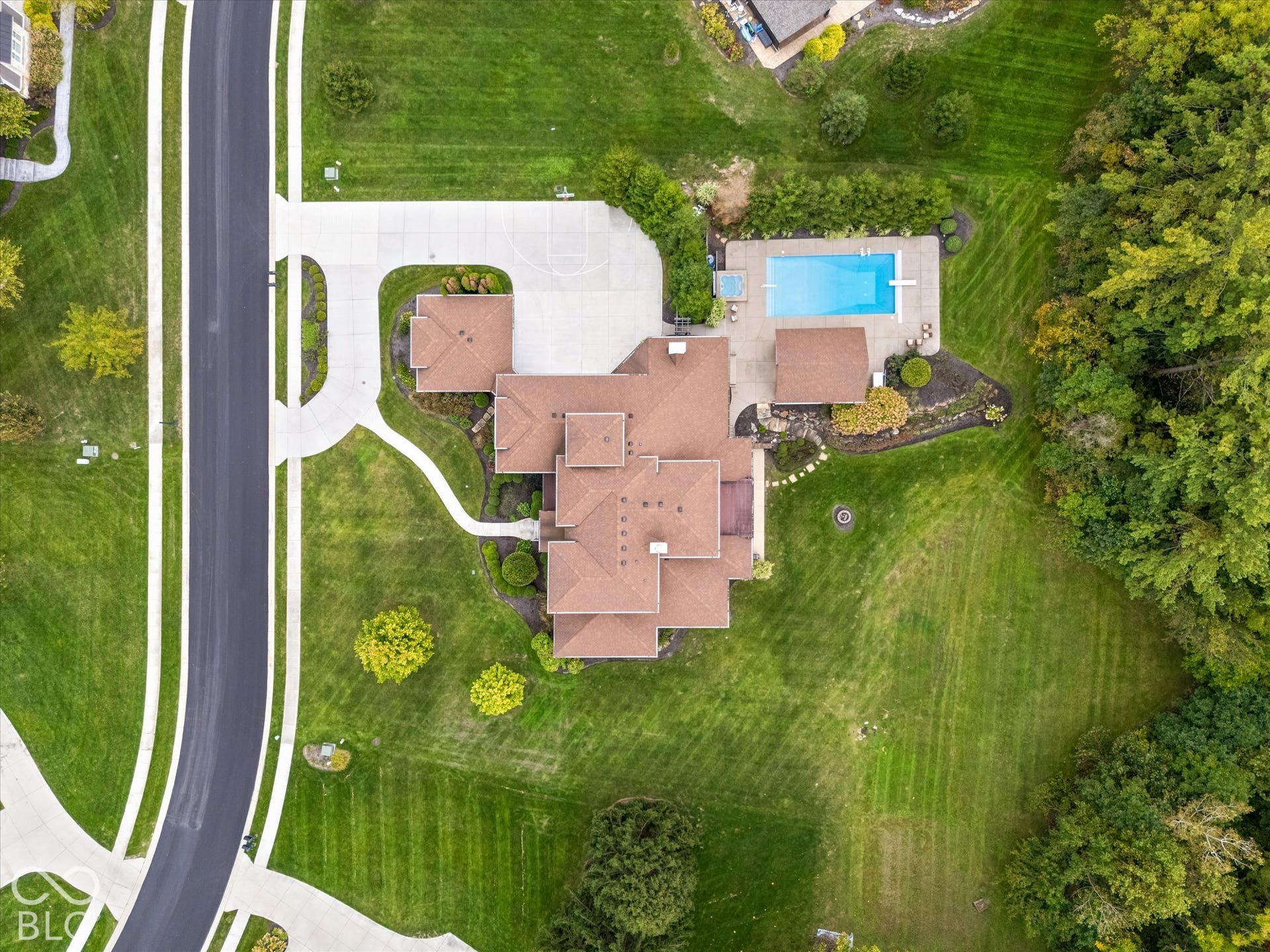Expansive property featuring a multi-level roofline, extensive paved driveway, private swimming pool with diving board, concrete sports court, and mature tree coverage