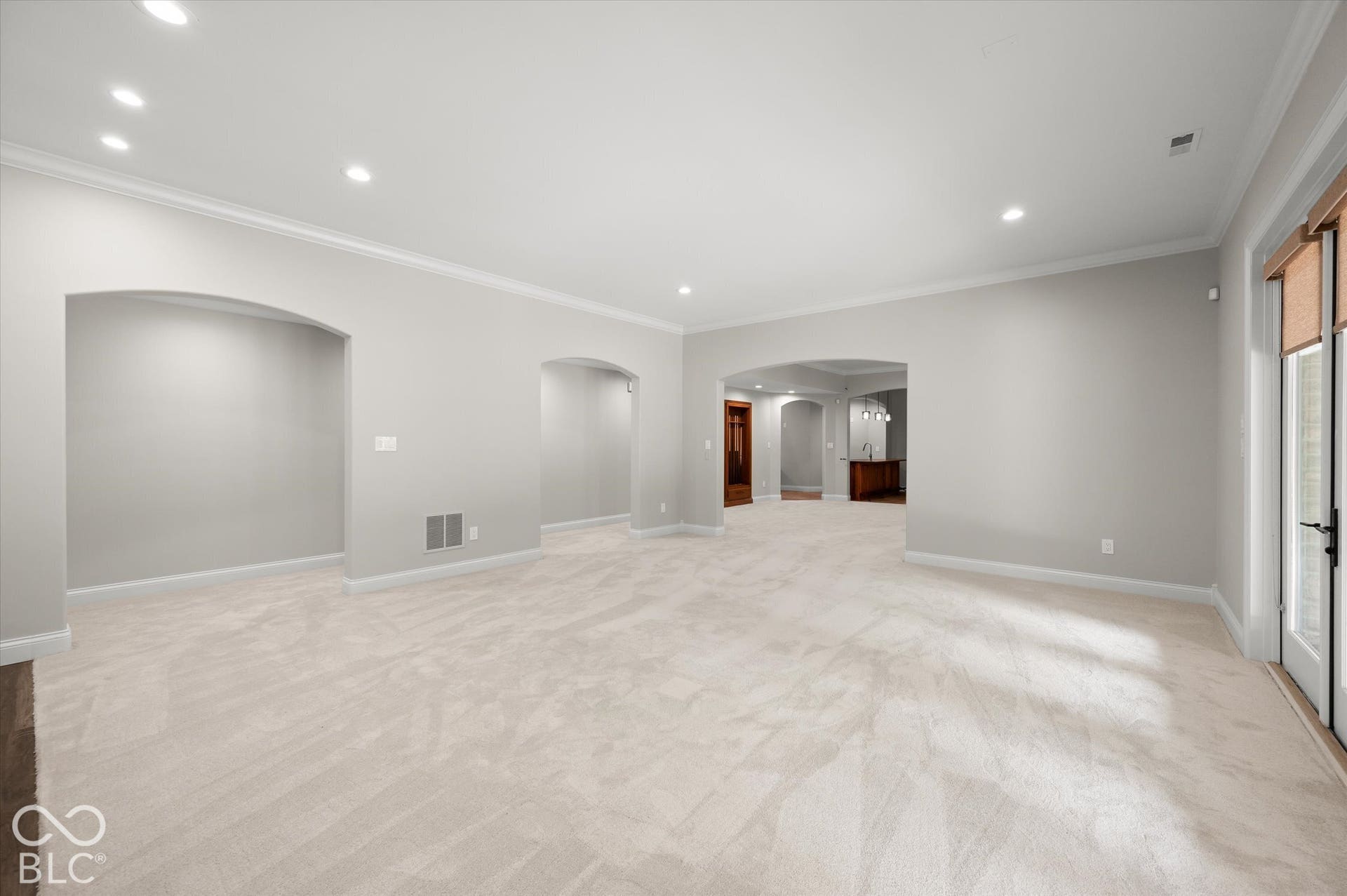 Light-colored carpeting, recessed lighting, arched doorways, crown molding, and a patio door with integrated blinds
