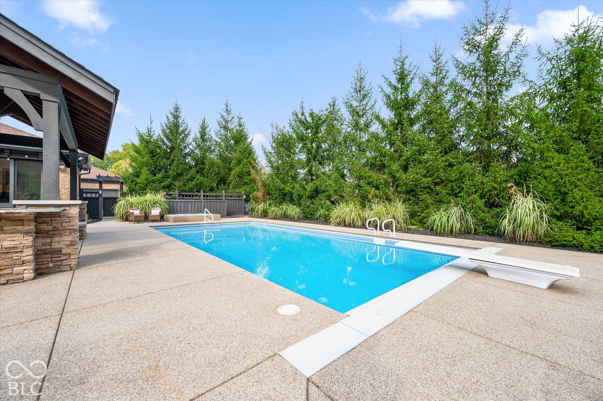 Rectangular in-ground swimming pool with a diving board, surrounded by an exposed aggregate concrete patio