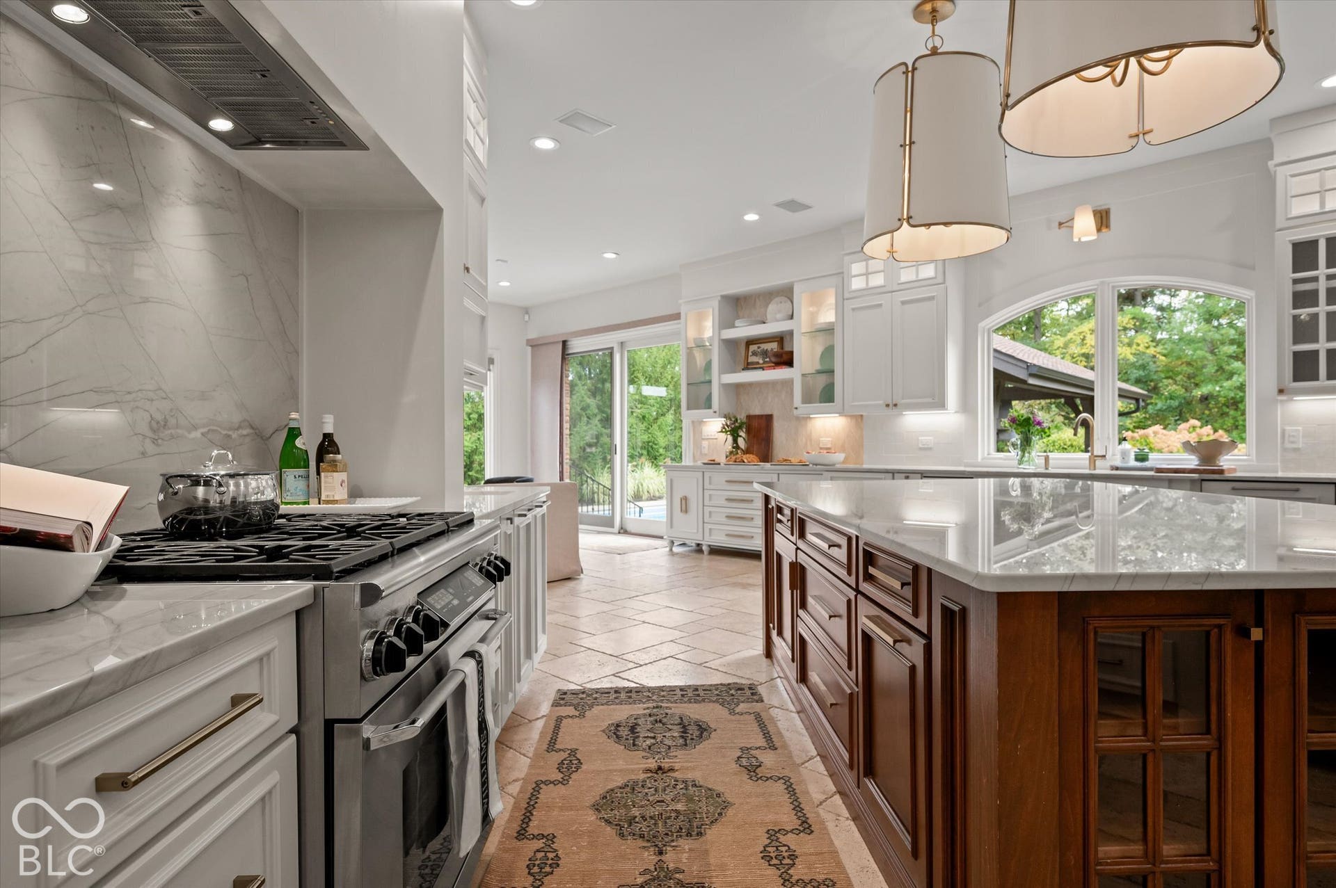 Stainless steel range with a ventilation hood, stone countertops, light cabinetry, a wood-finish kitchen island with a stone top, and arched windows