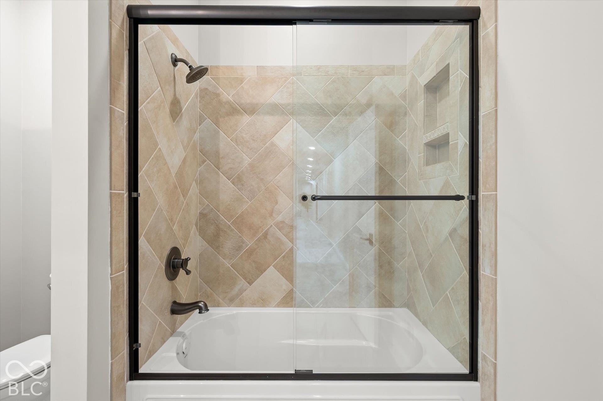 Bathtub with glass shower enclosure, herringbone tile surround, built-in shower niche, and dark bronze fixtures
