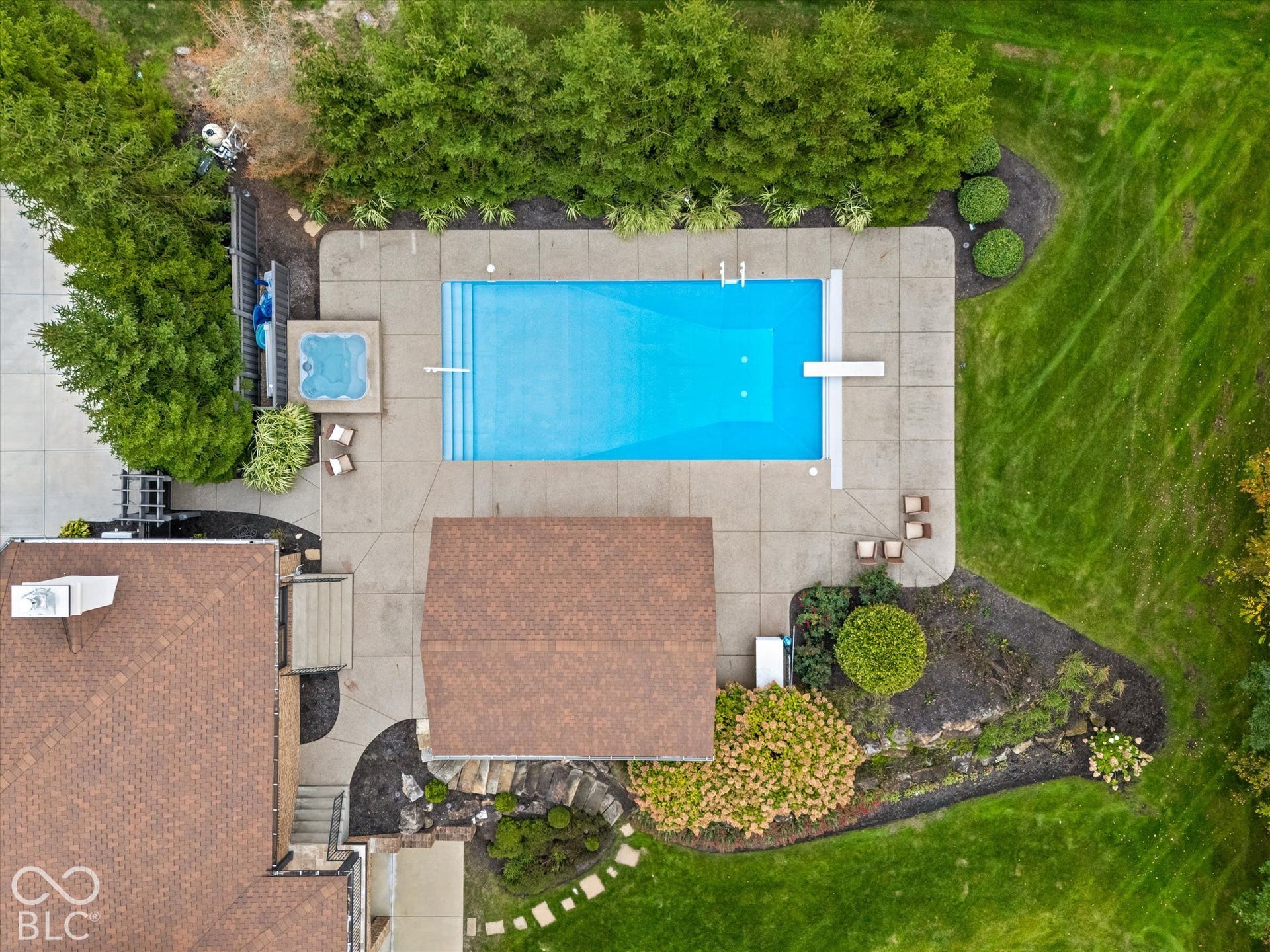 In-ground swimming pool with diving board, spa, and extensive concrete patio