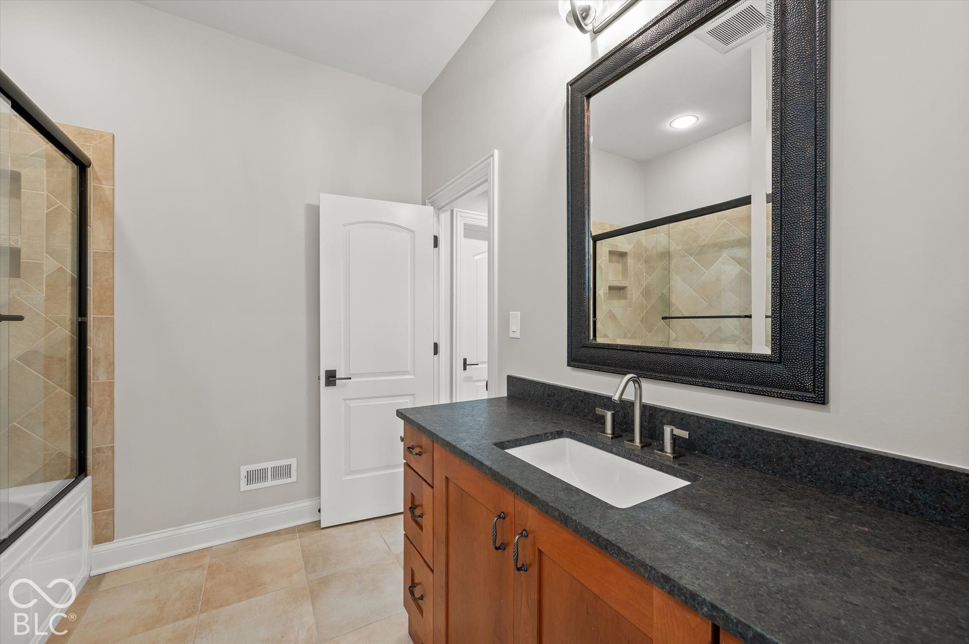 Spacious bathroom featuring a single vanity with a dark countertop, an undermount sink, and a framed mirror