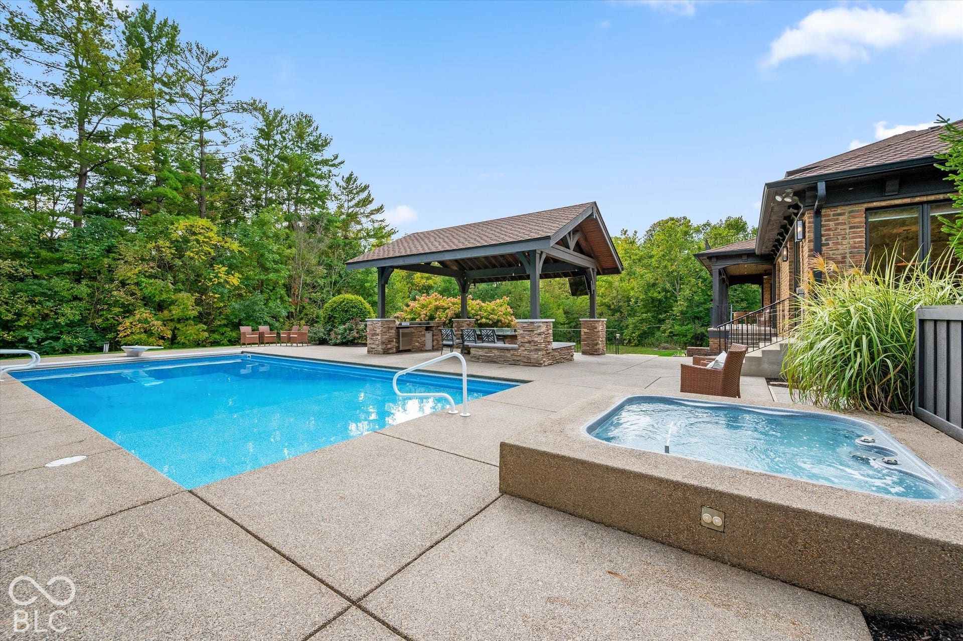 Expansive outdoor living area featuring a built-in swimming pool, integrated hot tub, and a covered outdoor kitchen with a stone-clad base