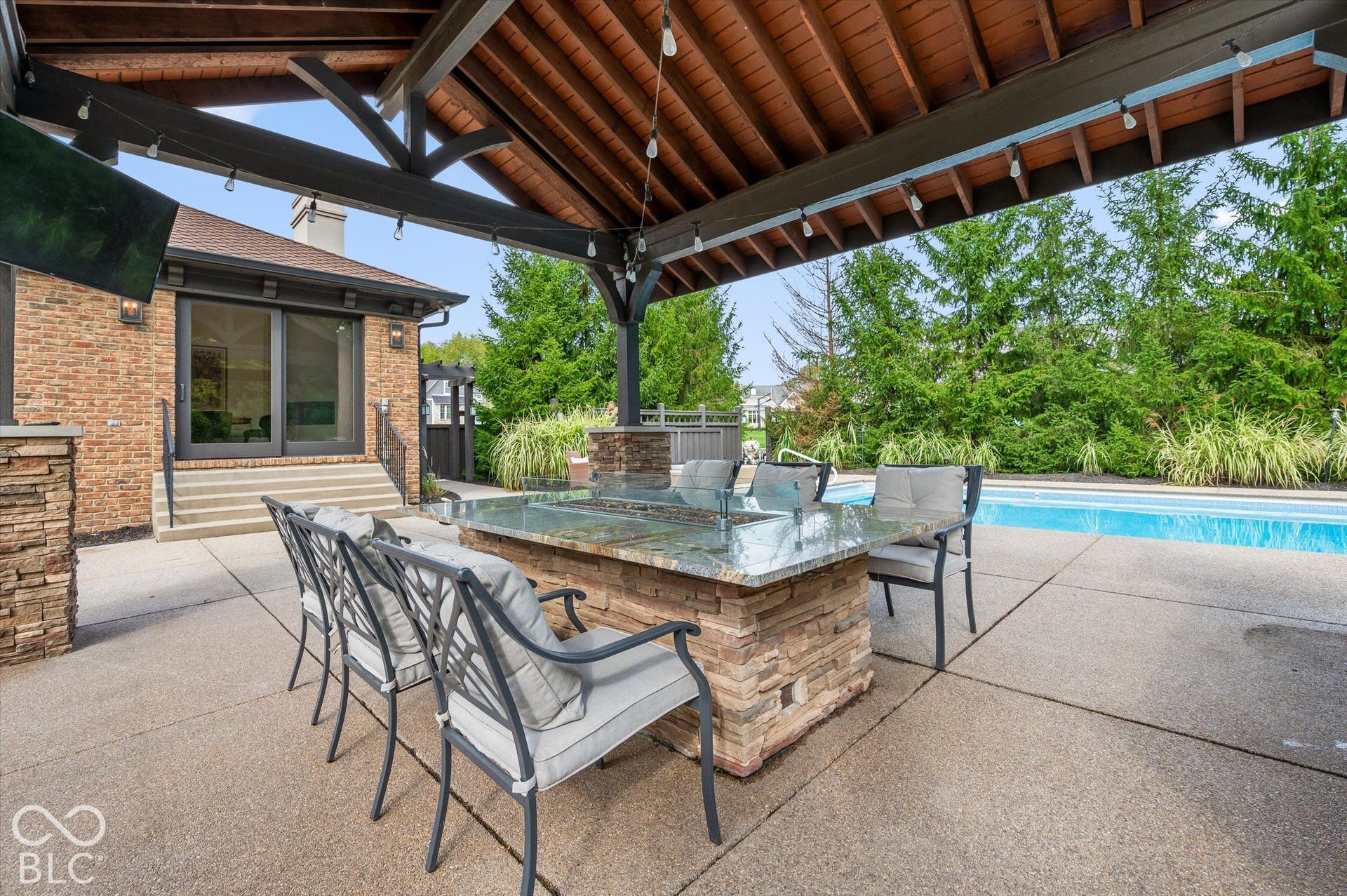 Covered outdoor entertaining area featuring a wood-plank ceiling, exposed beams, a built-in stone fire table, and a swimming pool