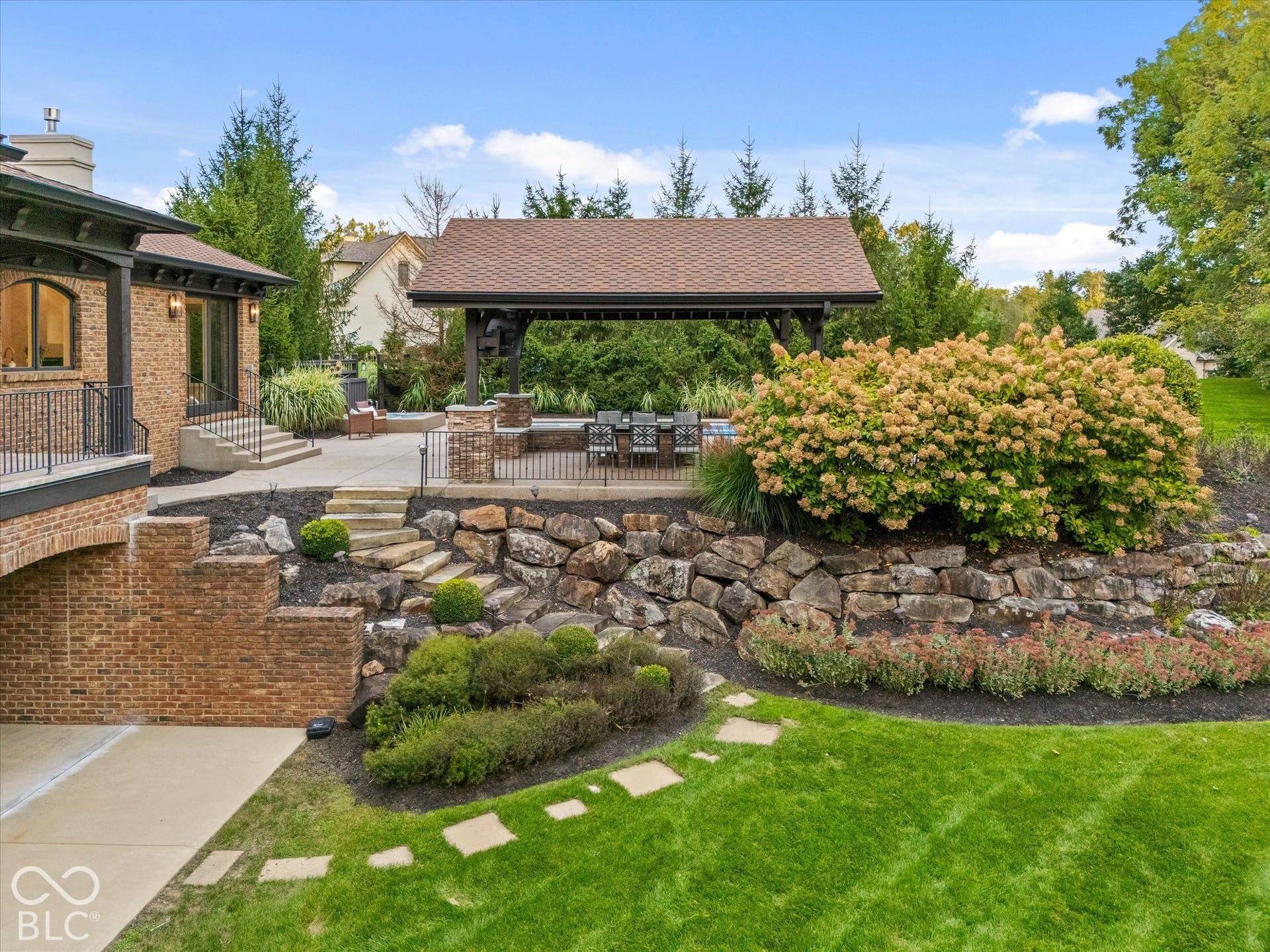 Expansive outdoor living area featuring a covered patio, tiered landscaping with stone retaining walls, and a manicured lawn
