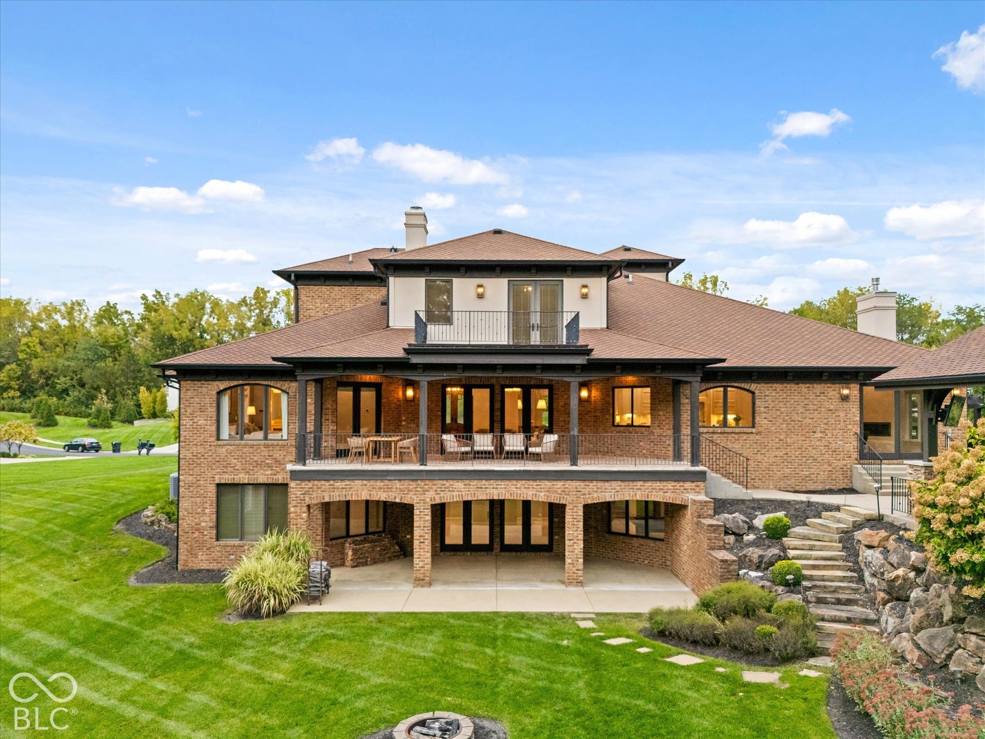 Brick exterior featuring multiple covered patios, a second-story balcony, and stepped landscaping