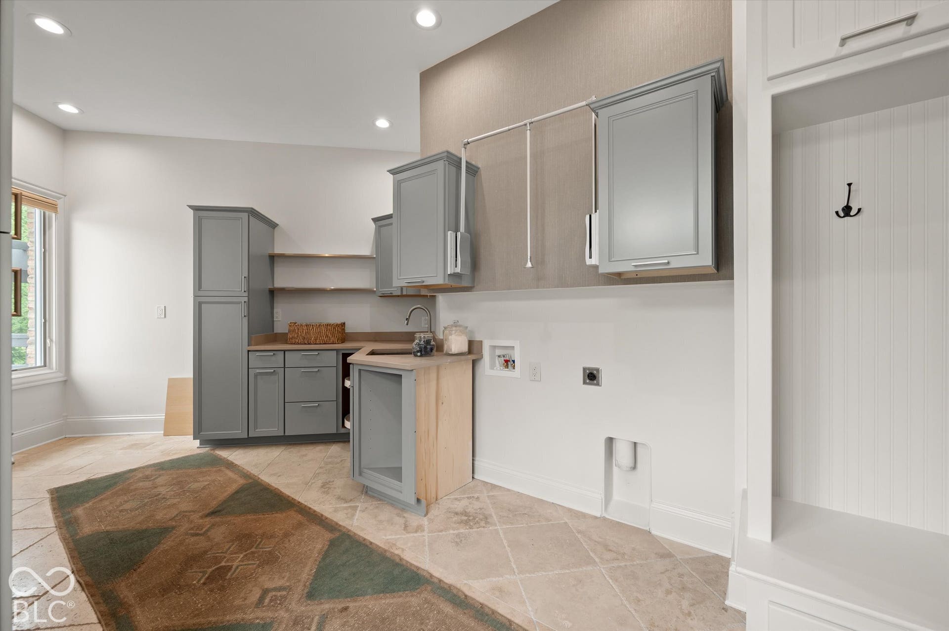 Integrated utility room featuring a built-in sink with a gooseneck faucet, gray cabinetry, open shelving, and neutral tile flooring