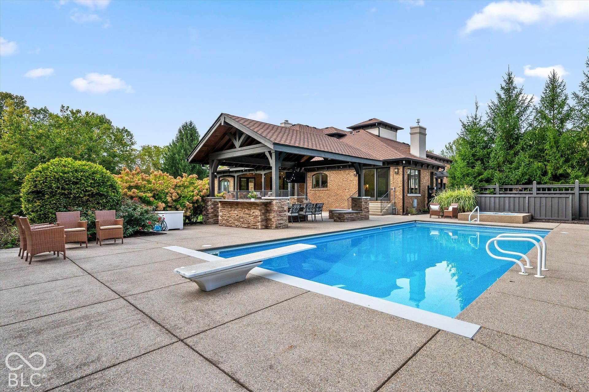 Expansive concrete patio surrounding a built-in swimming pool with a diving board and integrated spa