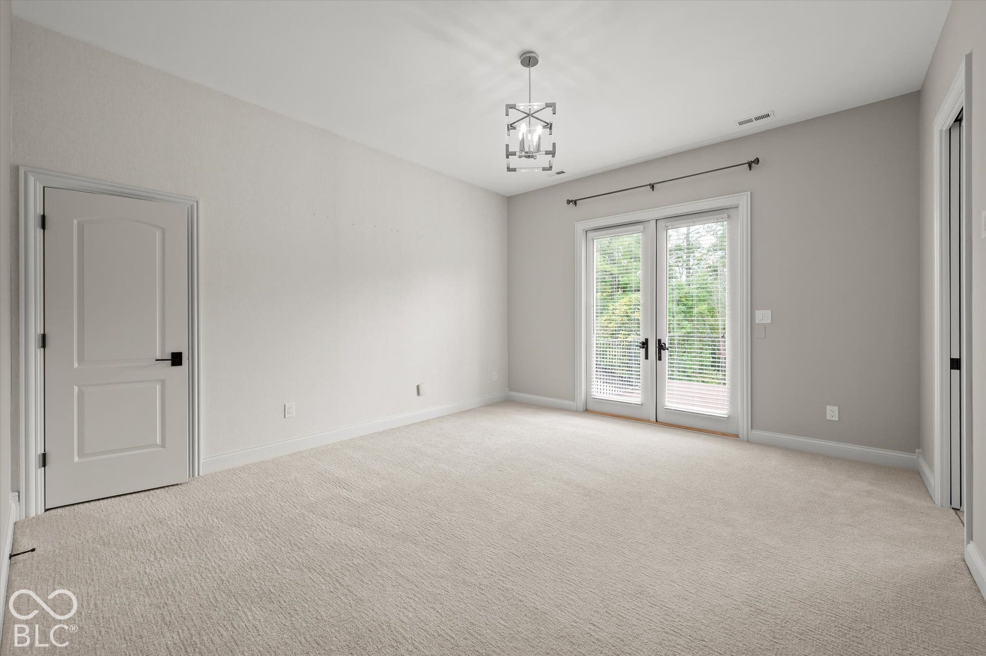 Neutral-toned carpeting, double French doors, contemporary chandelier, and arched panel doors with matte black hardware