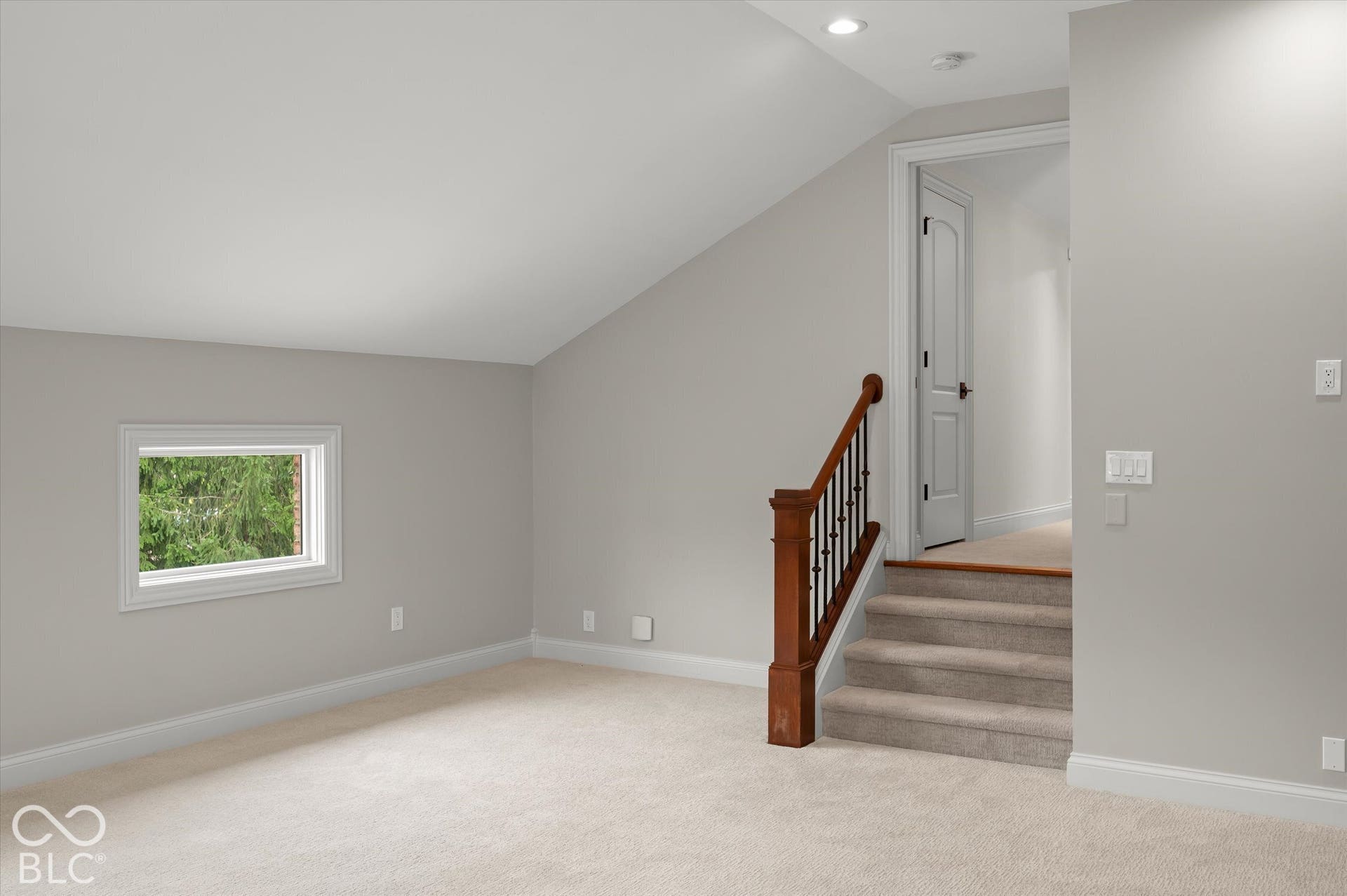 Carpeted room featuring a white-framed window, sloped ceiling, recessed lighting, and a wood and iron baluster staircase