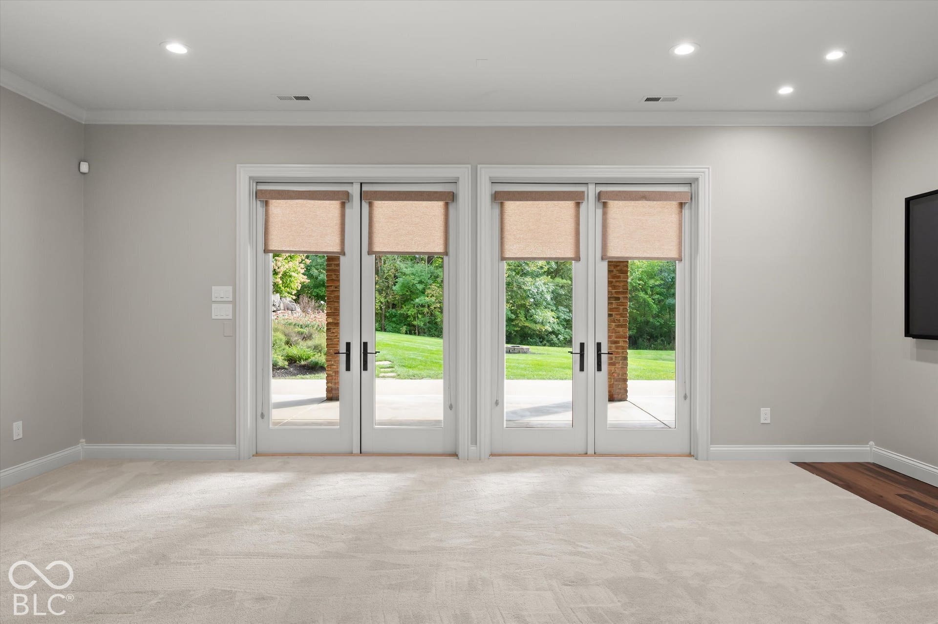 Two sets of French doors with roller shades, recessed lighting, crown molding, light-toned carpet, and a partial wood-finish flooring accent